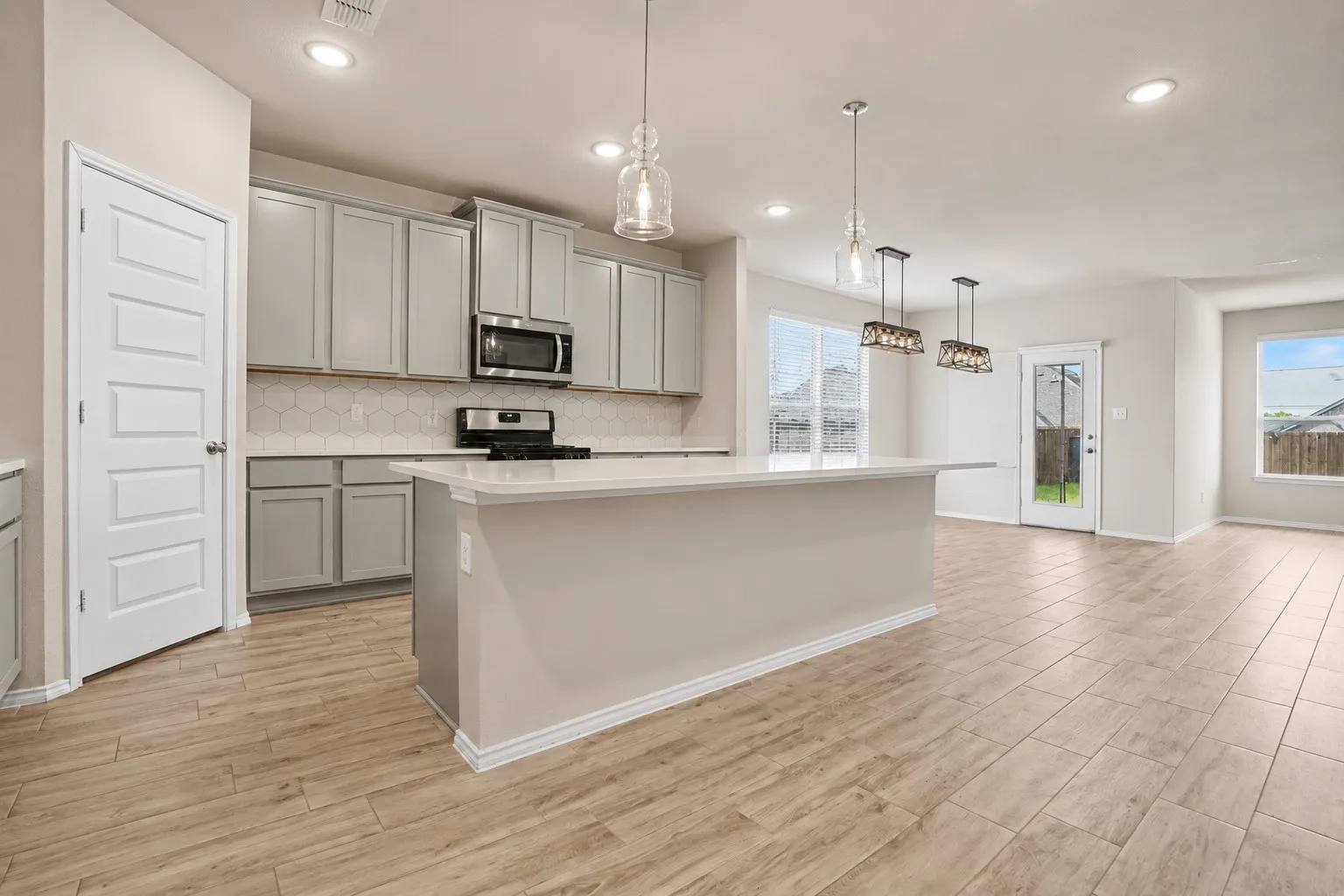 Kitchen featuring light gray cabinetry, white countertops, hexagonal tile backsplash, and stainless steel appliances