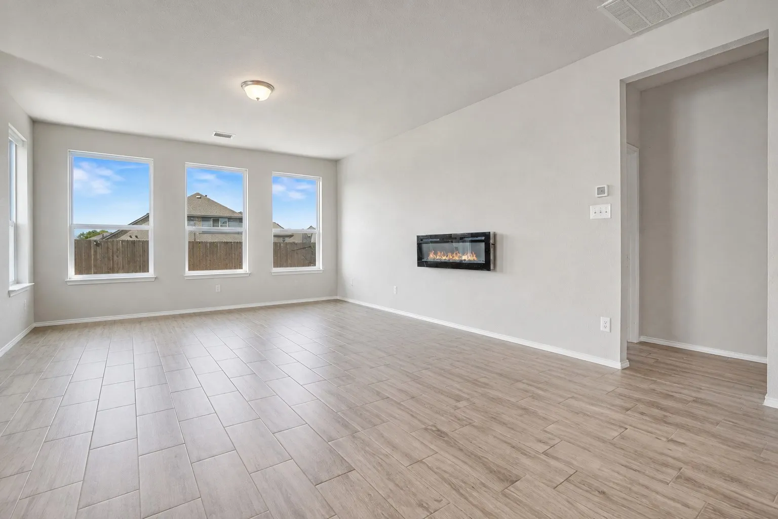 Recessed electric fireplace, three large windows, wood-finish flooring, light neutral wall color, and a flush-mount ceiling light