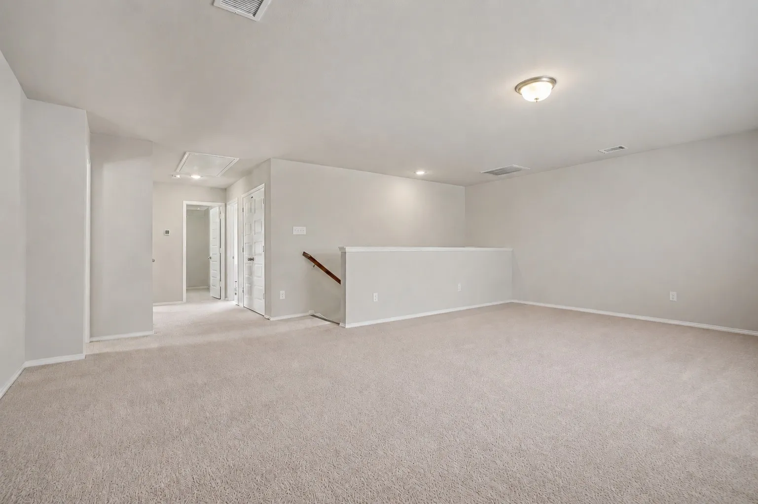 Spacious carpeted area with a half-wall partition, recessed lighting, and a flush mount ceiling fixture