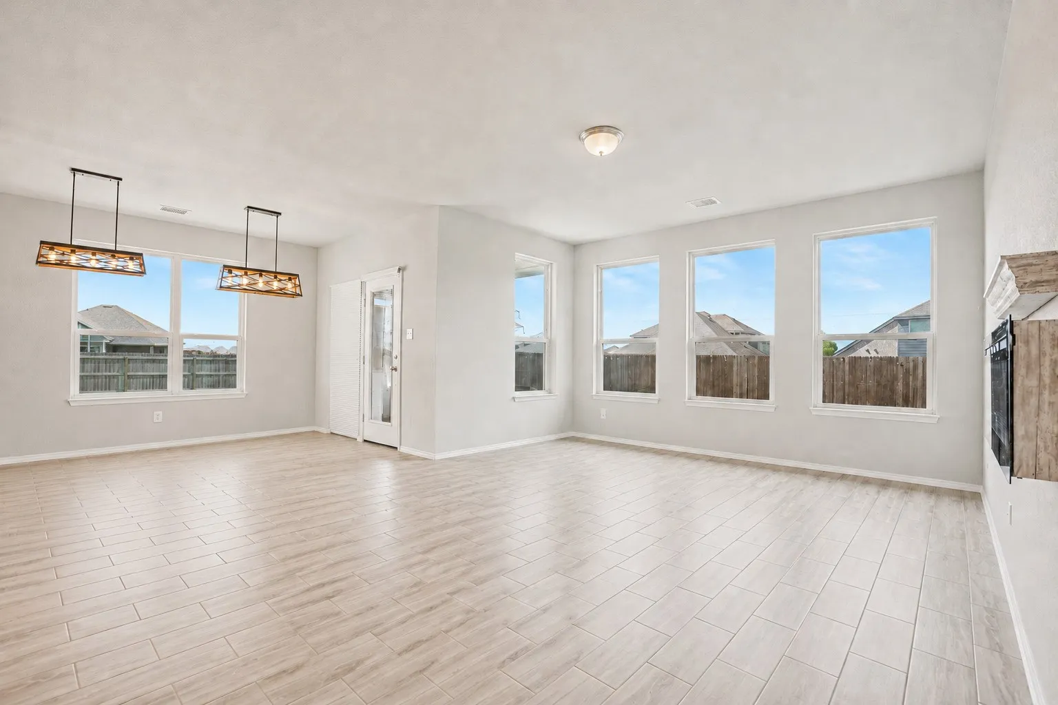 Expansive open-concept room featuring light-toned tile flooring, multiple windows, and two decorative pendant light fixtures