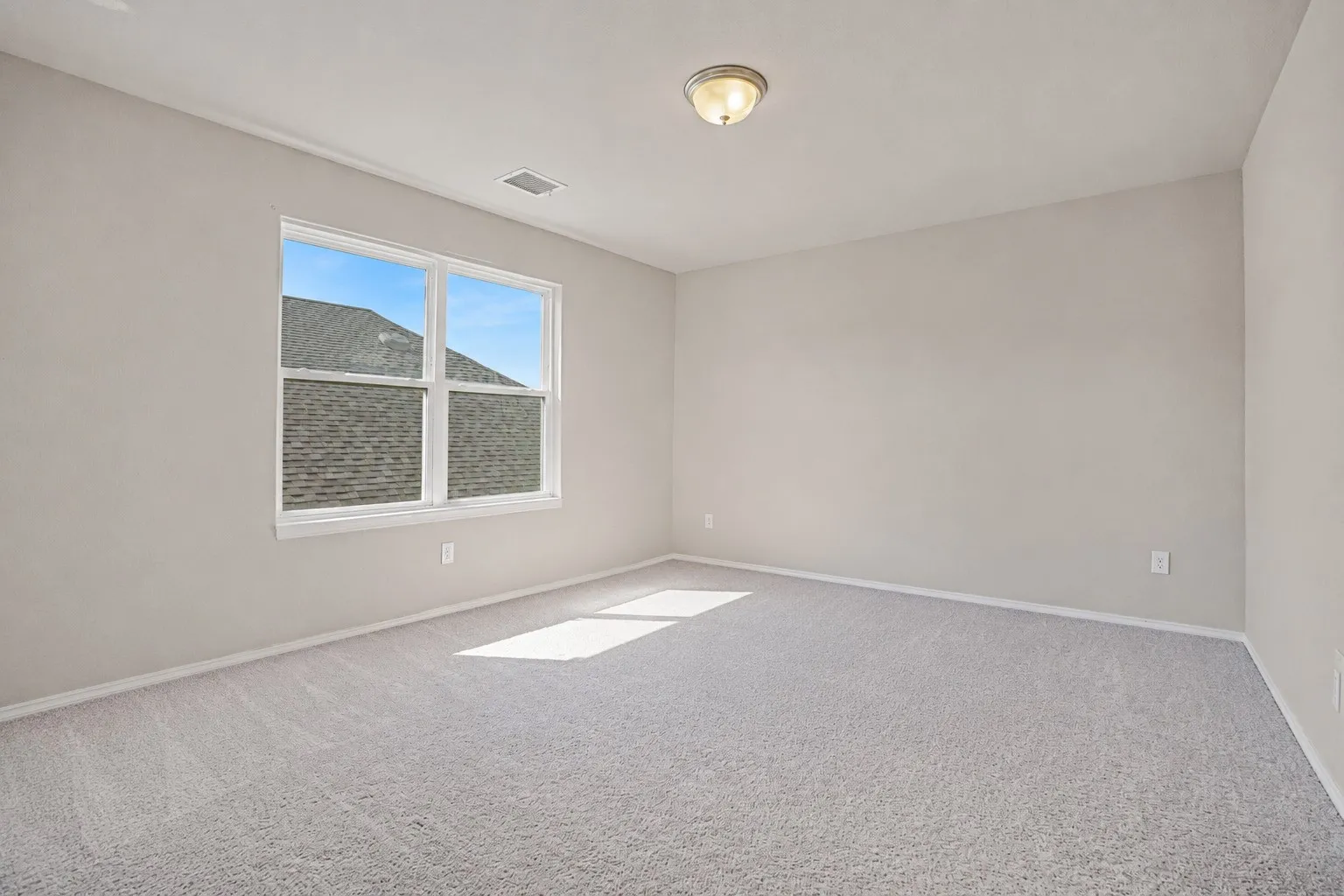 Neutral tone wall paint with light-colored carpeting, featuring a large window with white trim, and a ceiling-mounted light fixture