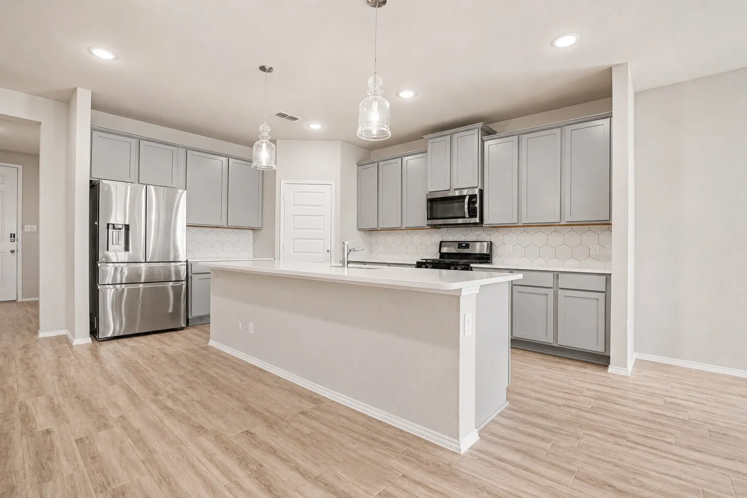 Kitchen featuring an island, light gray cabinetry, stainless steel appliances, hexagonal tile backsplash, and recessed lighting