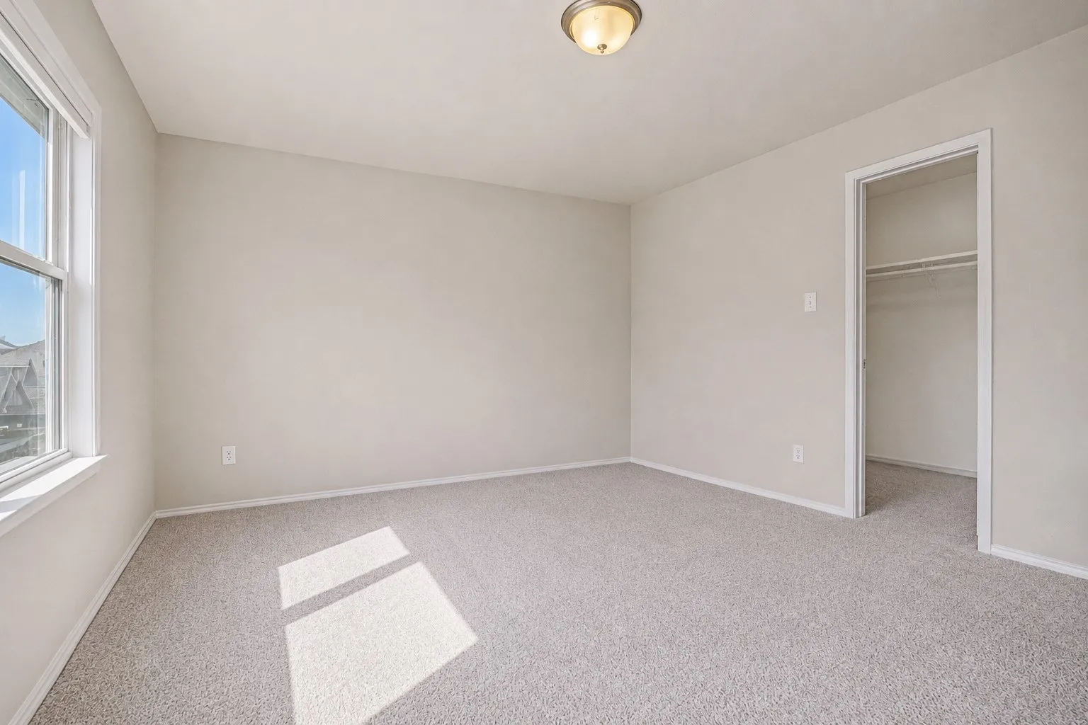 Carpeted room featuring a double-hung window, flush mount ceiling light, and an open closet with shelving and a clothes rod