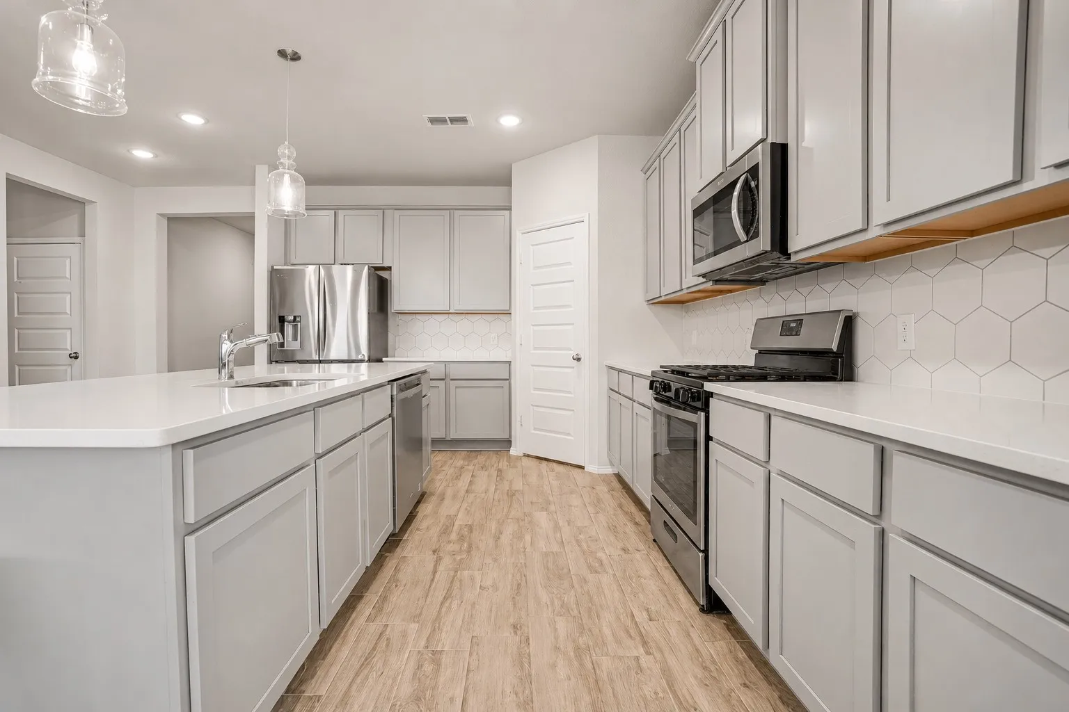 Kitchen featuring light wood-finish flooring, white countertops, gray shaker-style cabinetry, and a hexagonal tile backsplash
