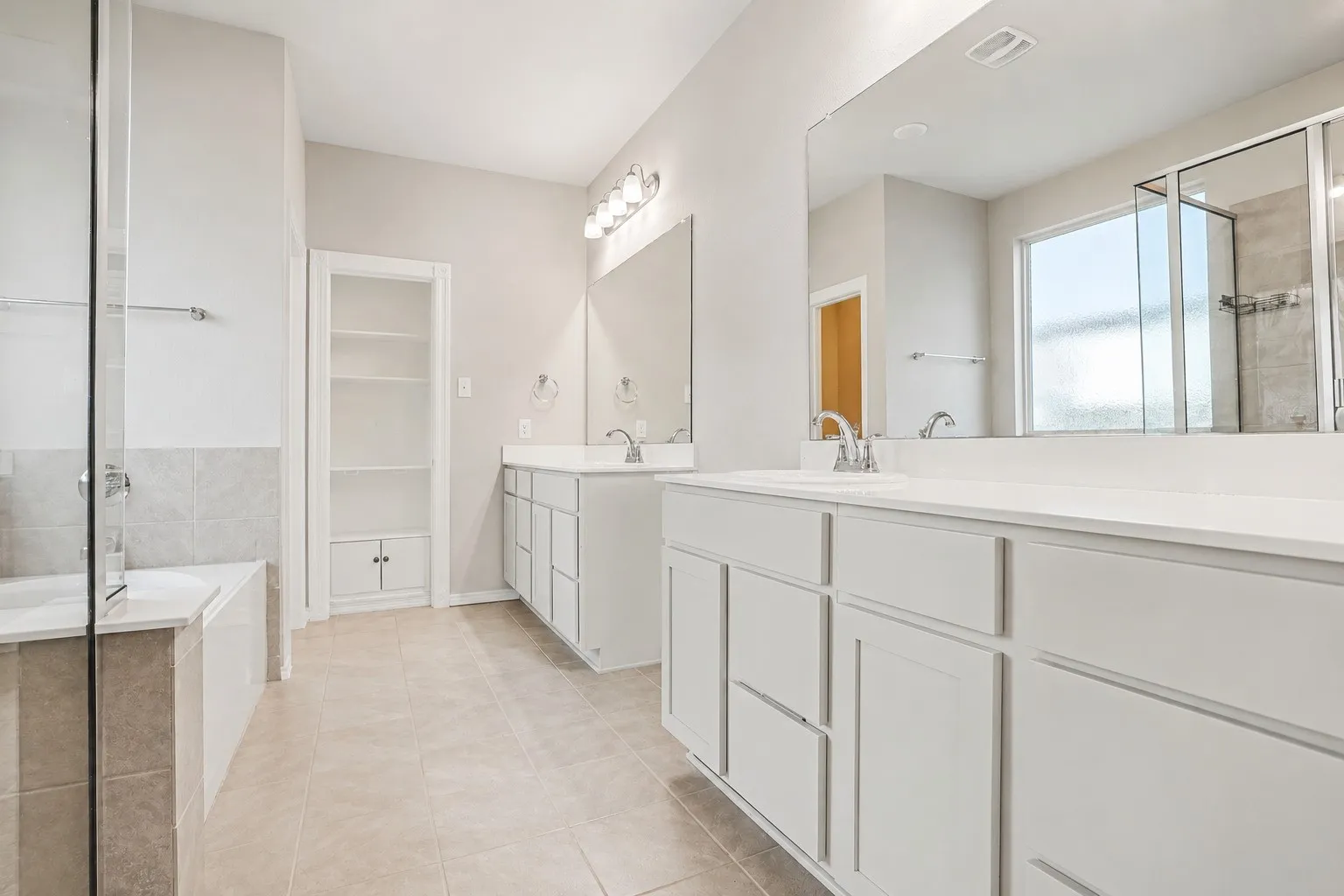 Dual vanity with white cabinetry and integrated sinks, a built-in shelving unit, a glass-enclosed shower, and a separate soaking tub with tiled surround