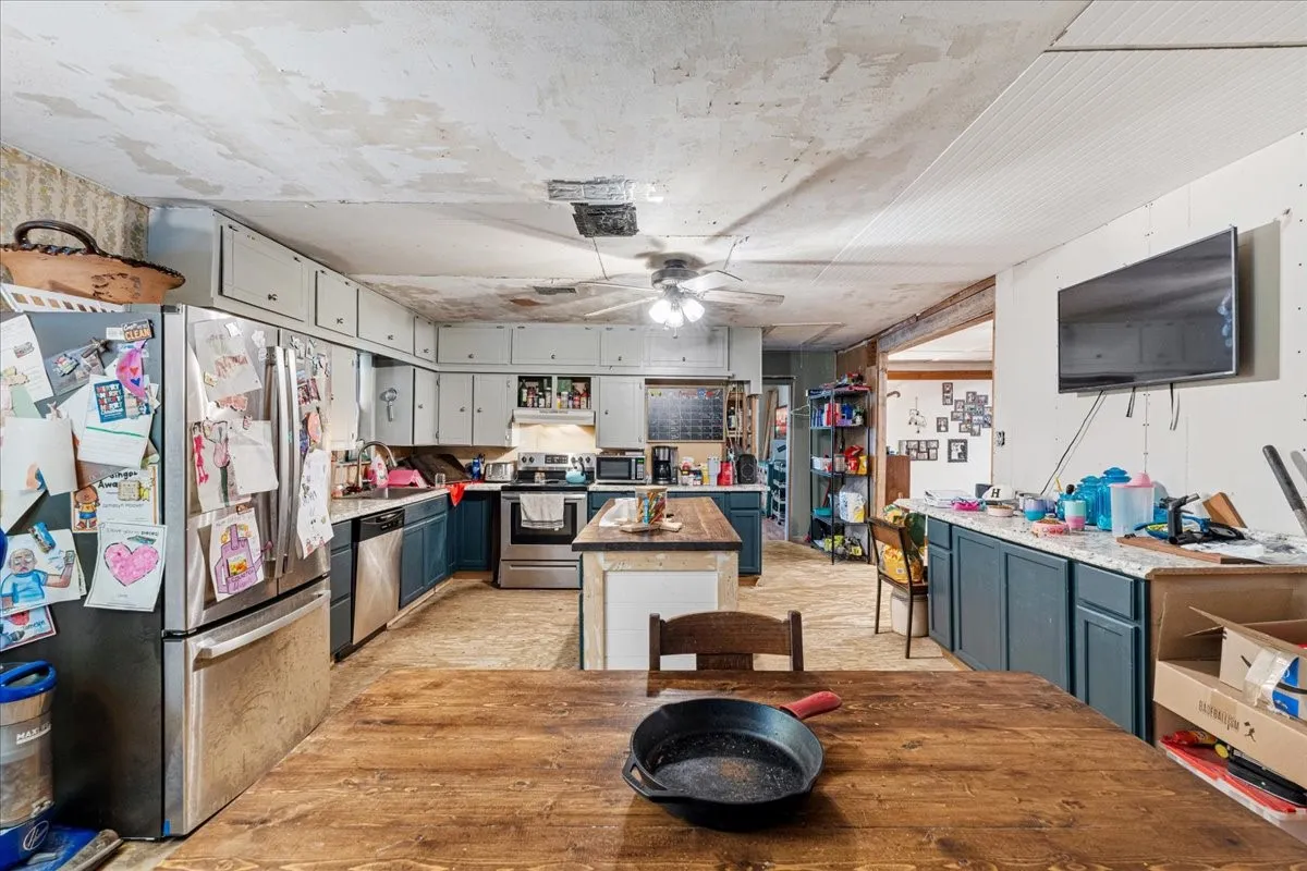Kitchen featuring stainless steel appliances, dual-tone cabinetry, a ceiling fan, a kitchen island, and wood-finish flooring