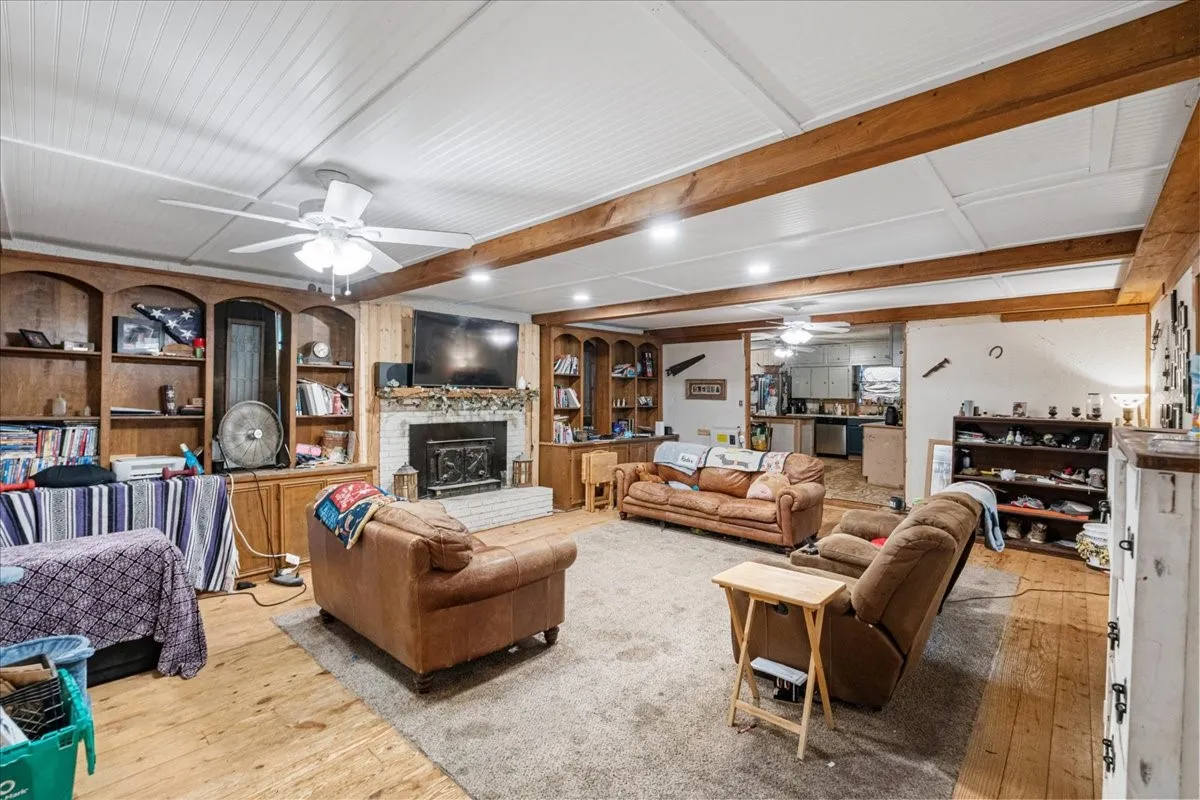 Exposed wood beams, beadboard ceiling, built-in shelving, wood-finish flooring, and a white brick fireplace
