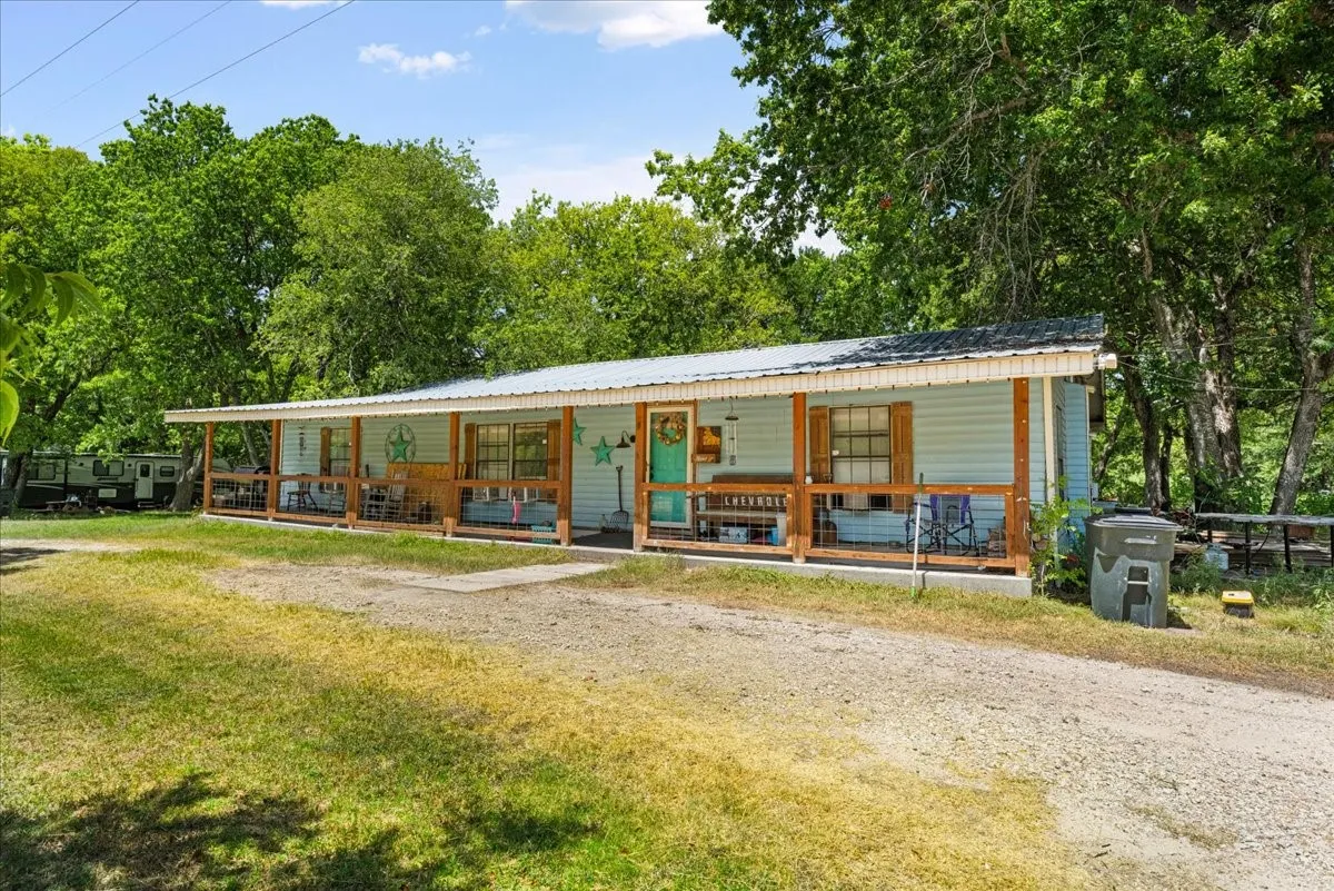 Light blue siding exterior with a wraparound wood porch, white trim, and a metal roof