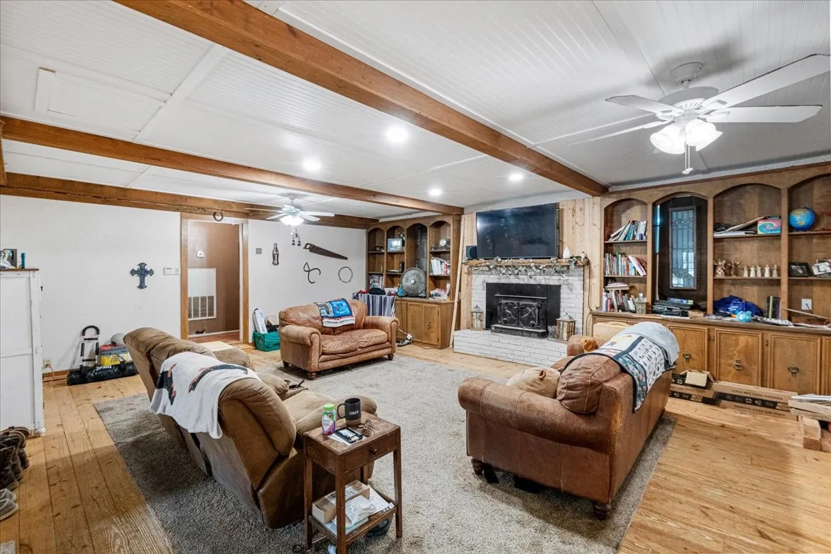 Exposed ceiling beams, beadboard ceiling, wood-finish flooring, brick fireplace with wood mantel, and built-in wood cabinetry