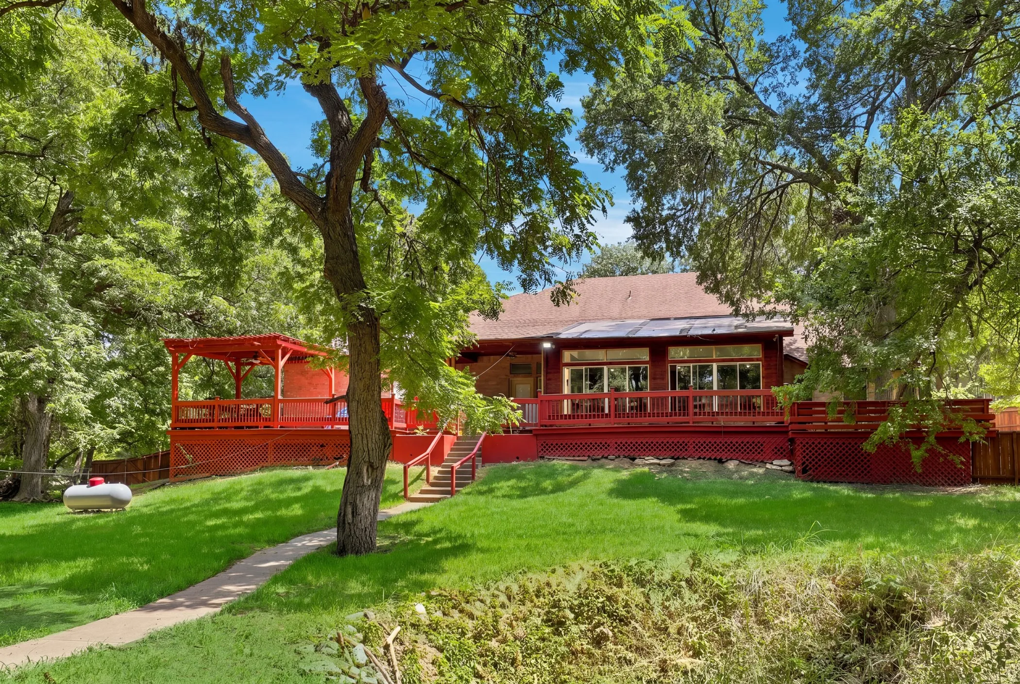 Expansive rear deck with red wood finish, offering a covered pergola and multiple steps to the yard