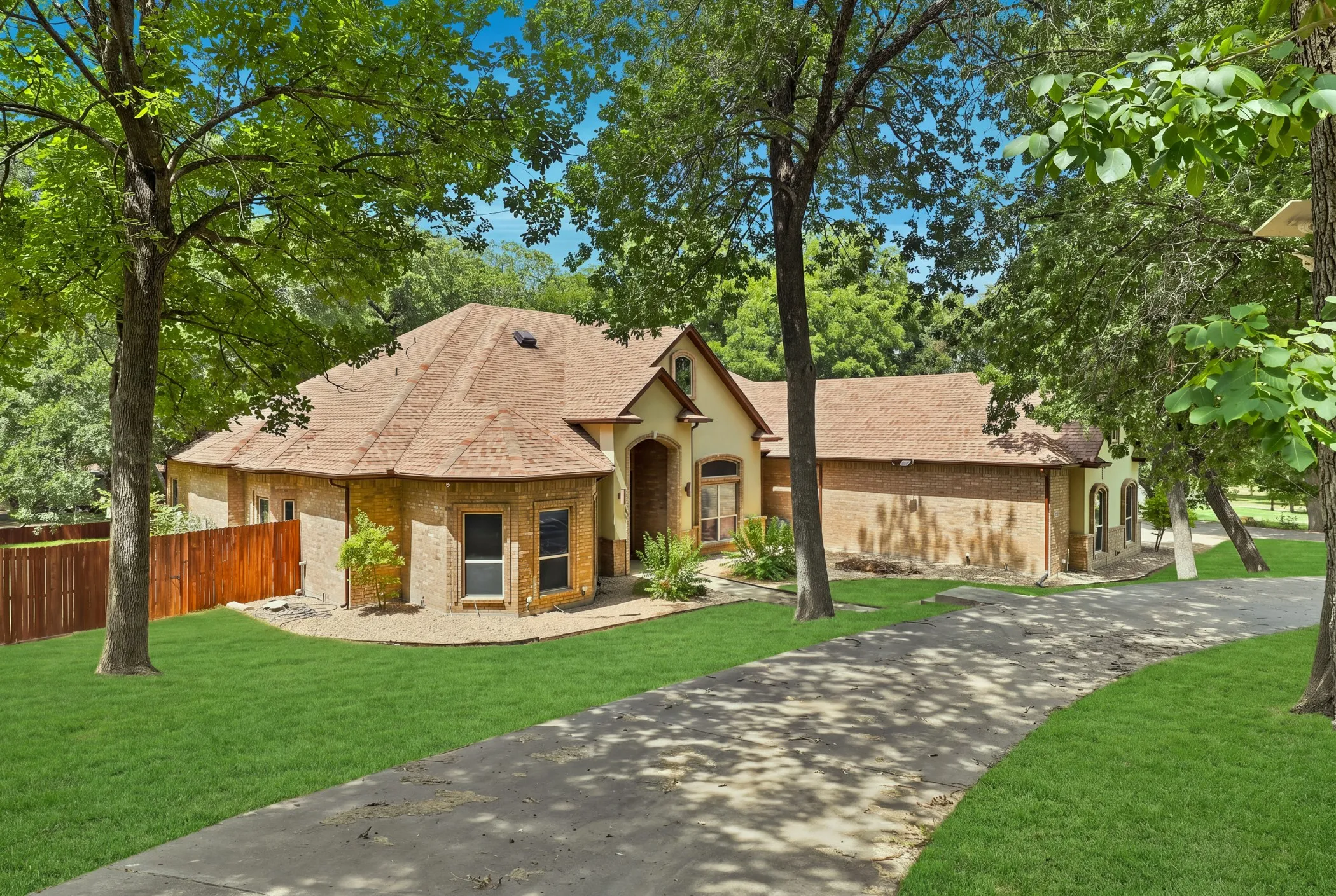 Traditional architecture with a brick and stucco exterior, featuring a private driveway, mature trees, and a wooden fence