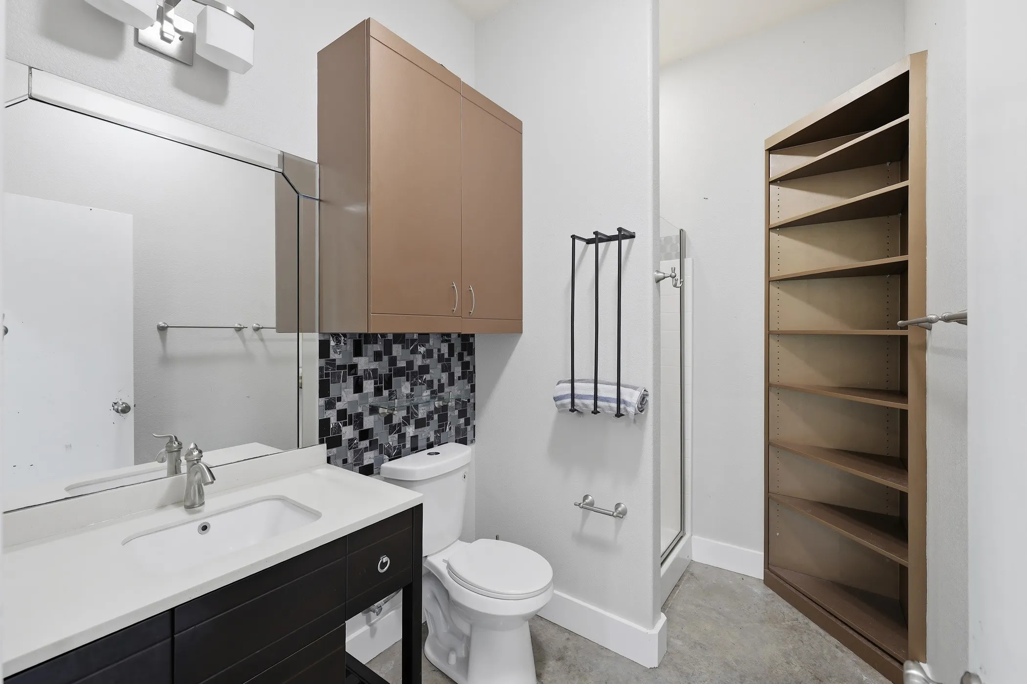 Vanity with an integrated sink and brushed nickel faucet, a mosaic tile accent wall, above-cabinet storage, and built-in shelving
