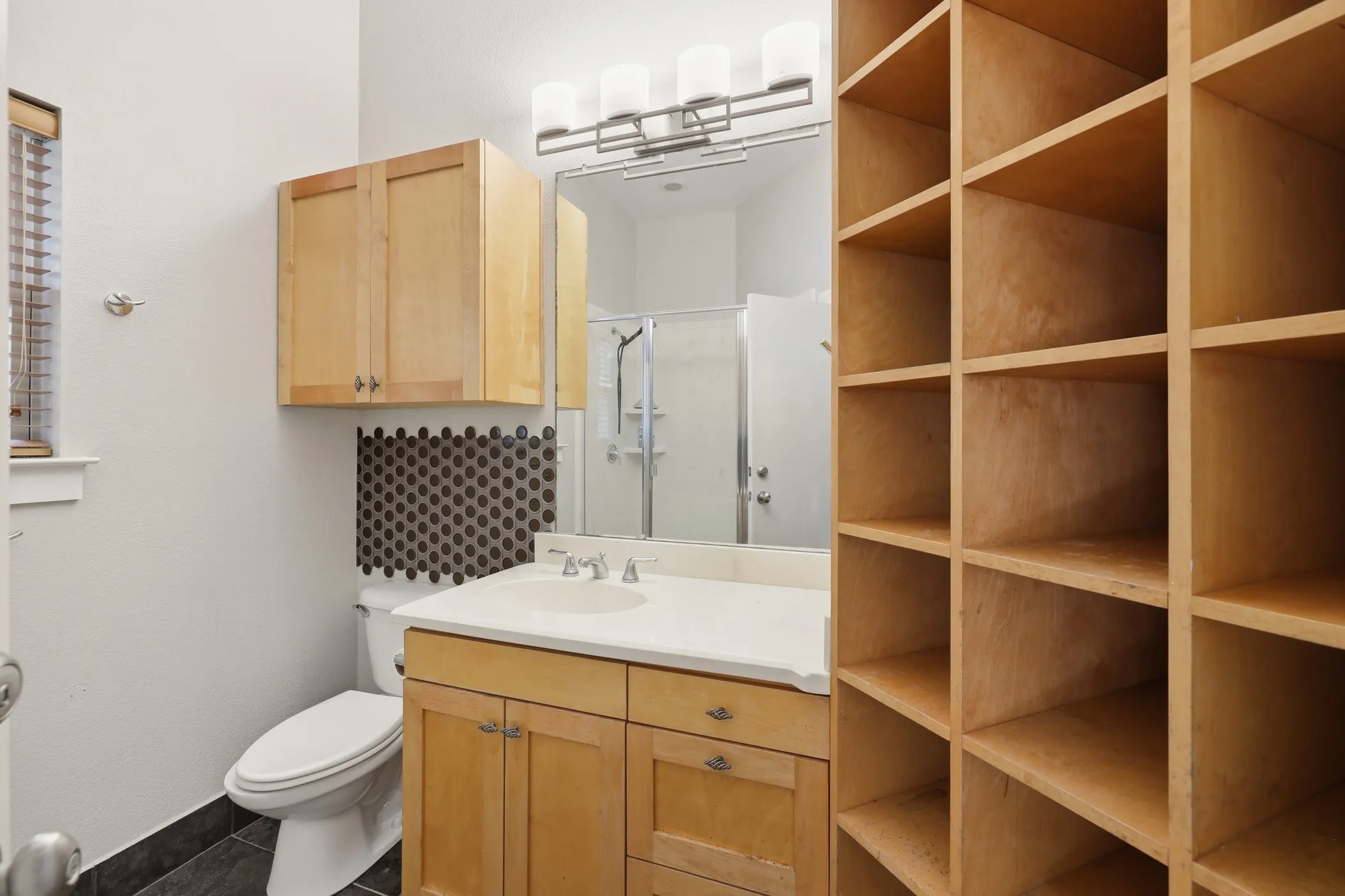 Built-in shelving, wood cabinetry, vanity with integrated sink, contemporary lighting, and tiled shower enclosure