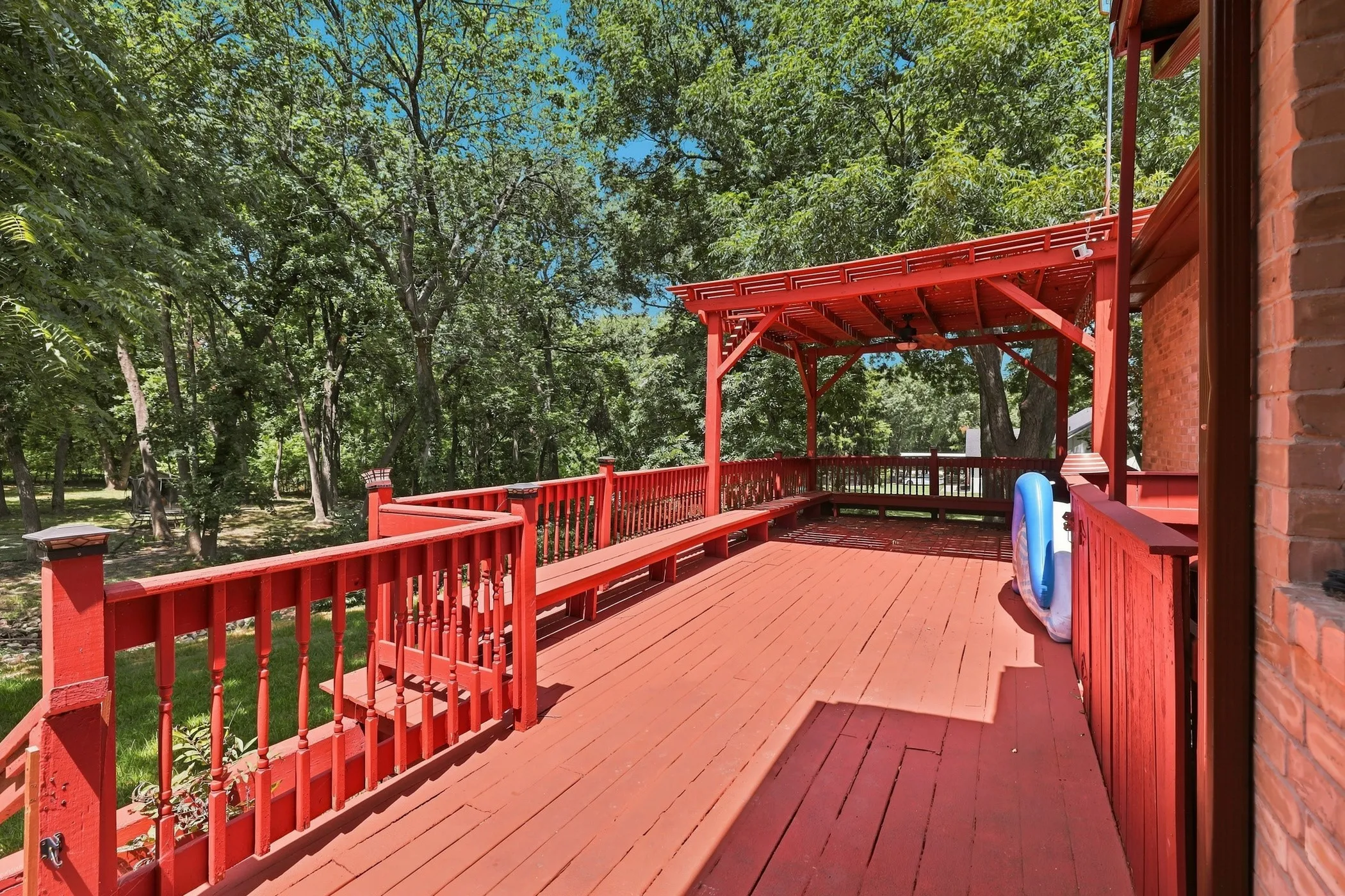 Expansive composite deck featuring rich red-stained wood flooring, decorative railings with turned balusters, and integrated pergola structure