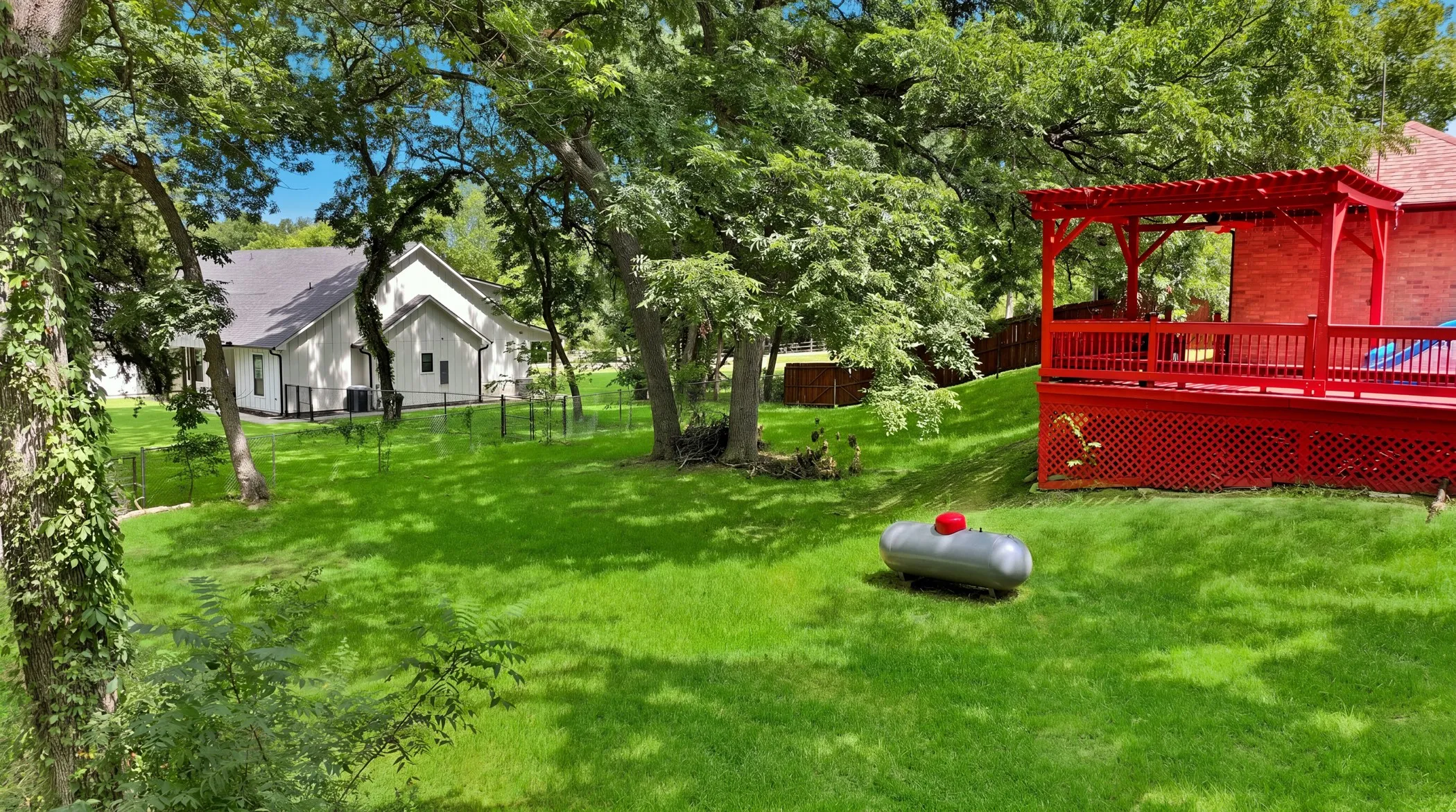 Expansive green lawn with mature trees, featuring a vibrant red deck and pergola