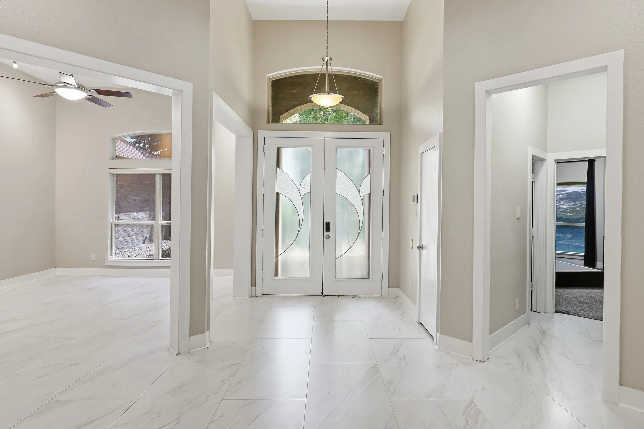 Vaulted entryway with double front doors featuring decorative glass panels, natural stone-finish flooring throughout, and an upper arched transom window