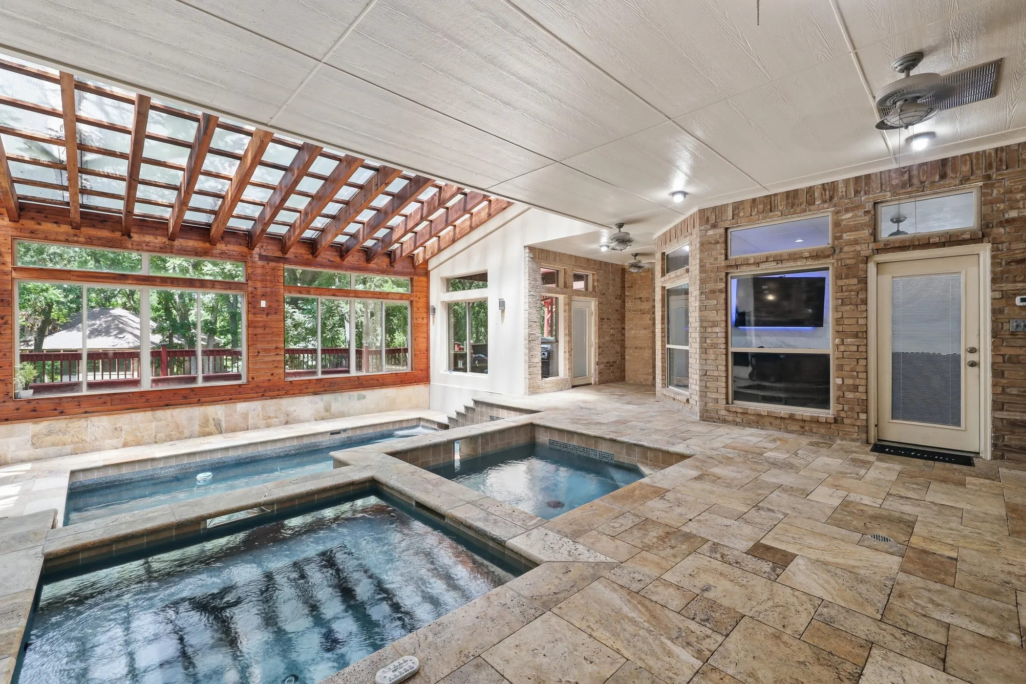 Indoor pool area featuring multiple integrated spas, extensive stone tile flooring, and a wood pergola ceiling