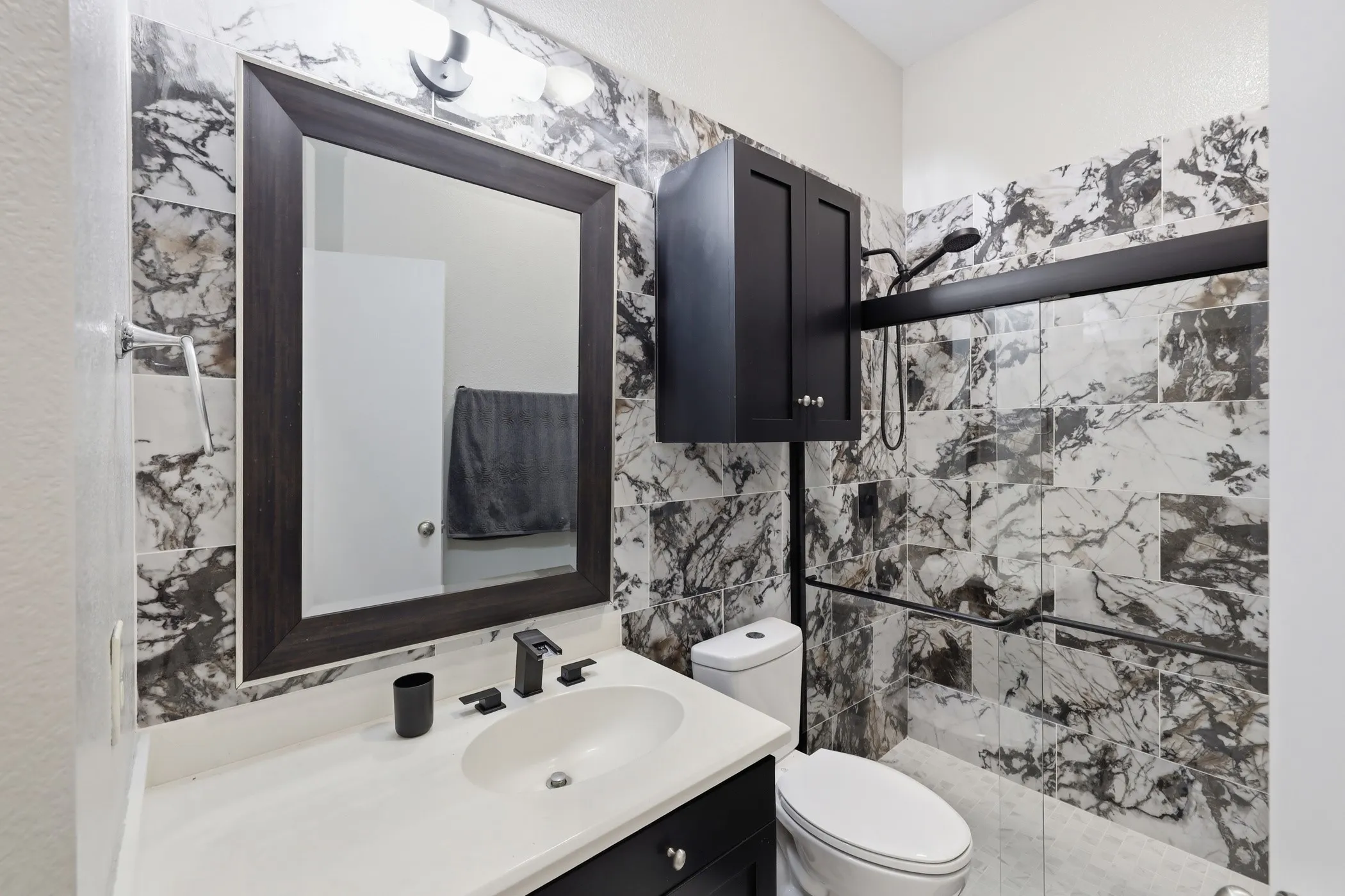 Bathroom featuring a dark wood-finish framed mirror, white countertop, black cabinetry, and patterned wall tiling