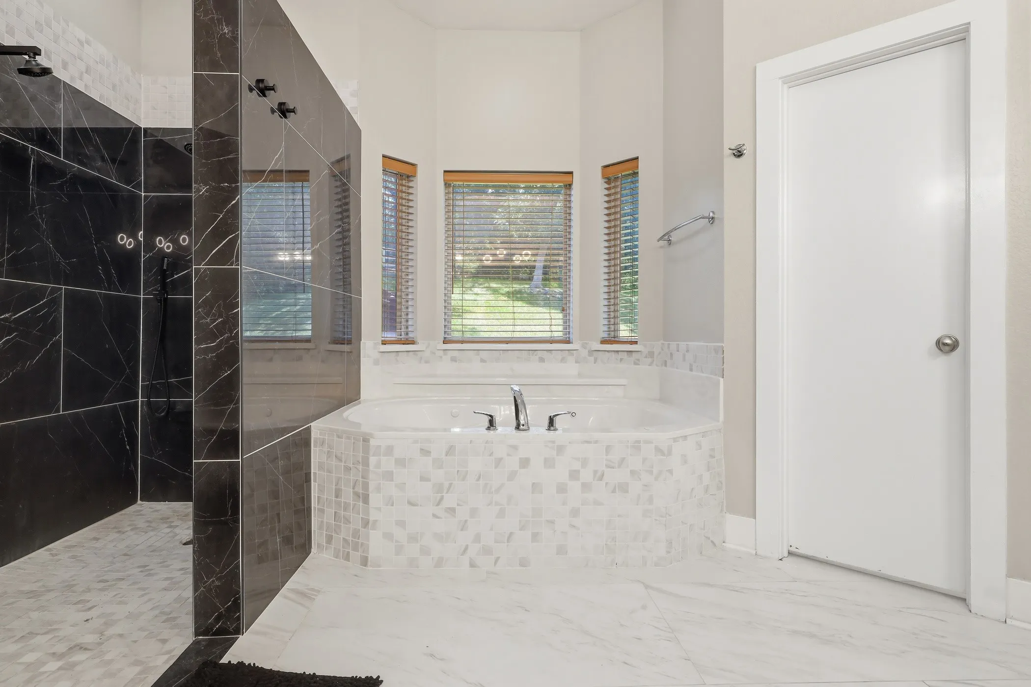 Walk-in shower with dark marbled tile, soaking tub with mosaic tile surround, and light tile flooring