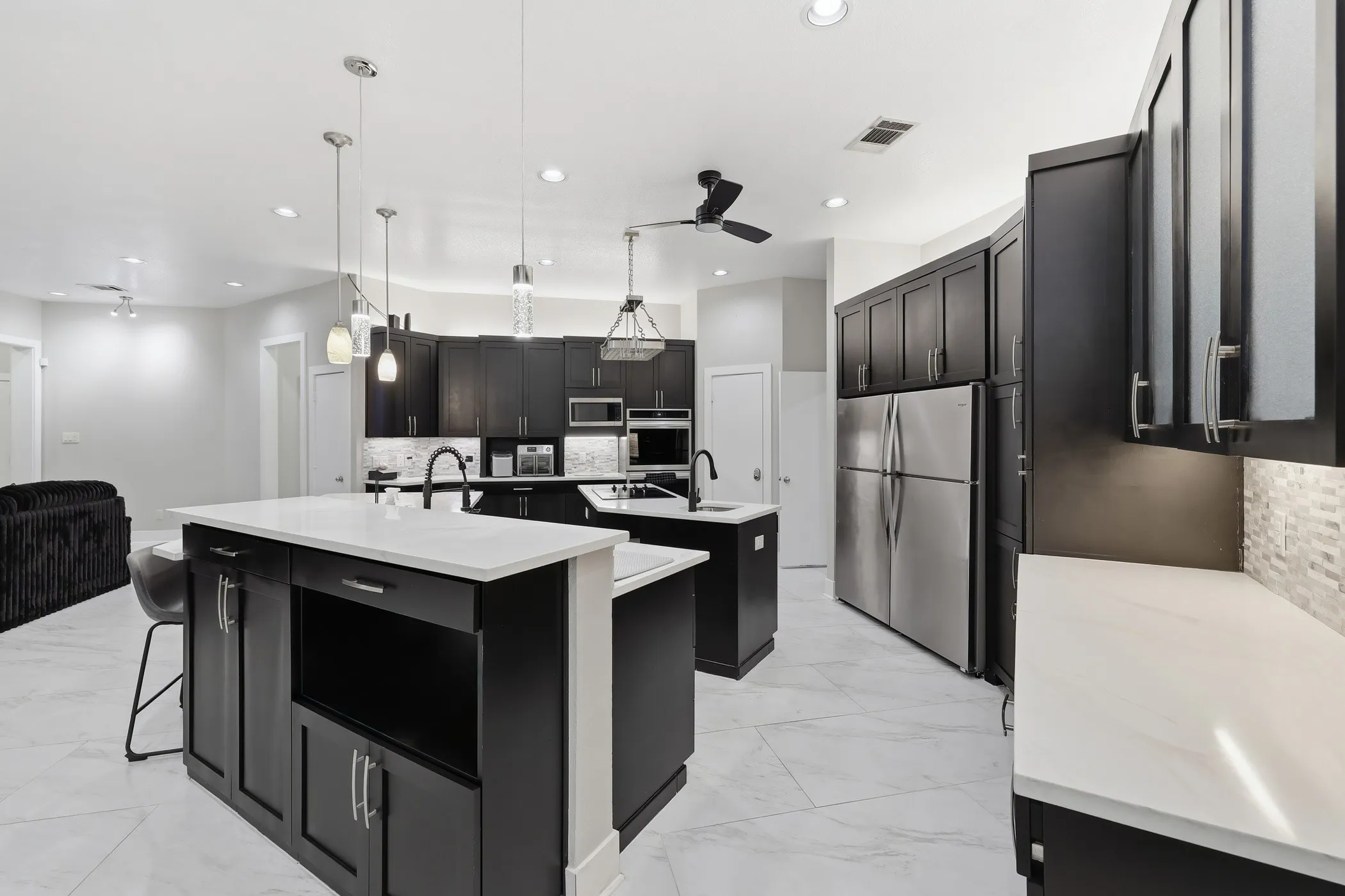Spacious kitchen featuring two islands with white countertops, dark cabinetry, stainless steel appliances, and recessed lighting