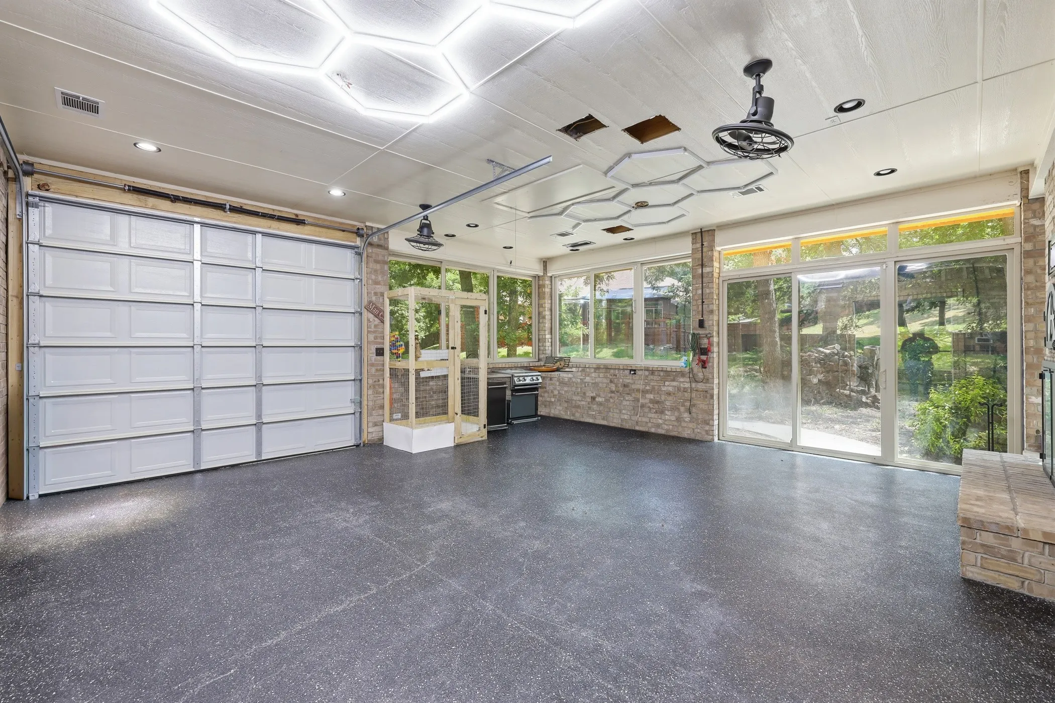 Spacious concrete-floor room featuring a large garage door, brick wall accents, and extensive windows with sliding glass doors