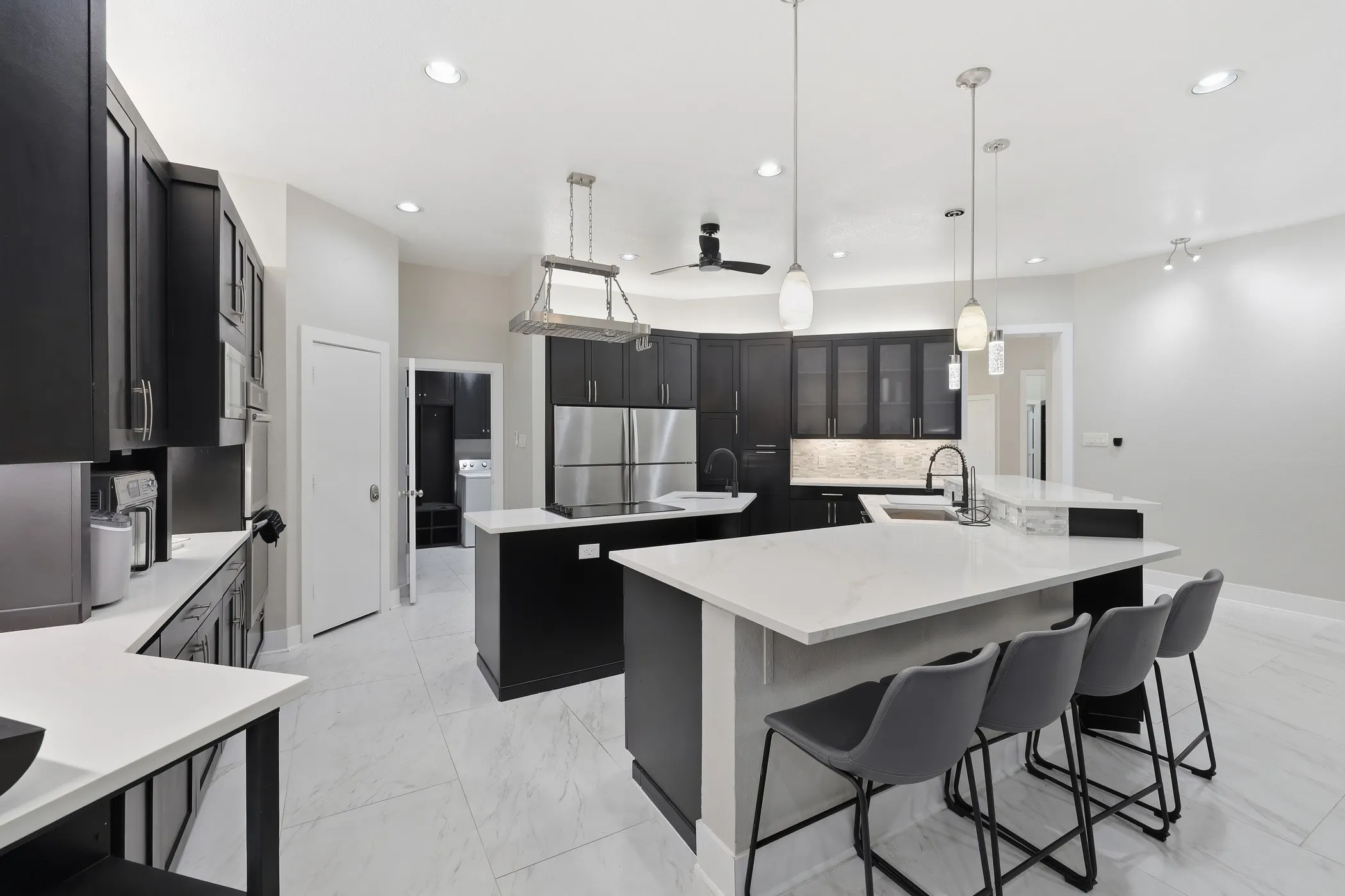 Modern kitchen featuring dark cabinetry, white countertops, two large kitchen islands, and integrated stainless steel appliances