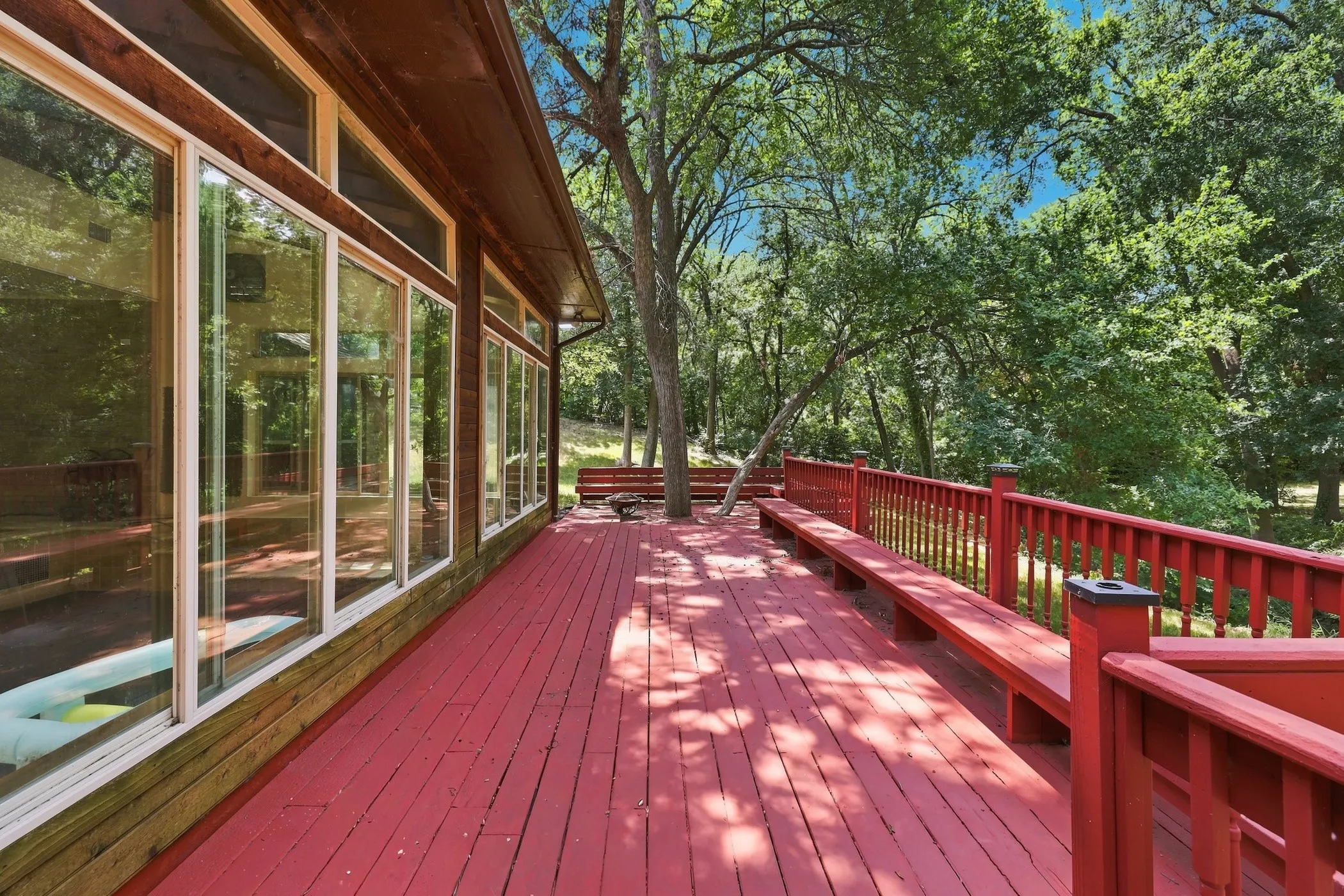 Expansive exterior deck featuring a red wood-finish surface, integrated bench seating, and a full-height railing