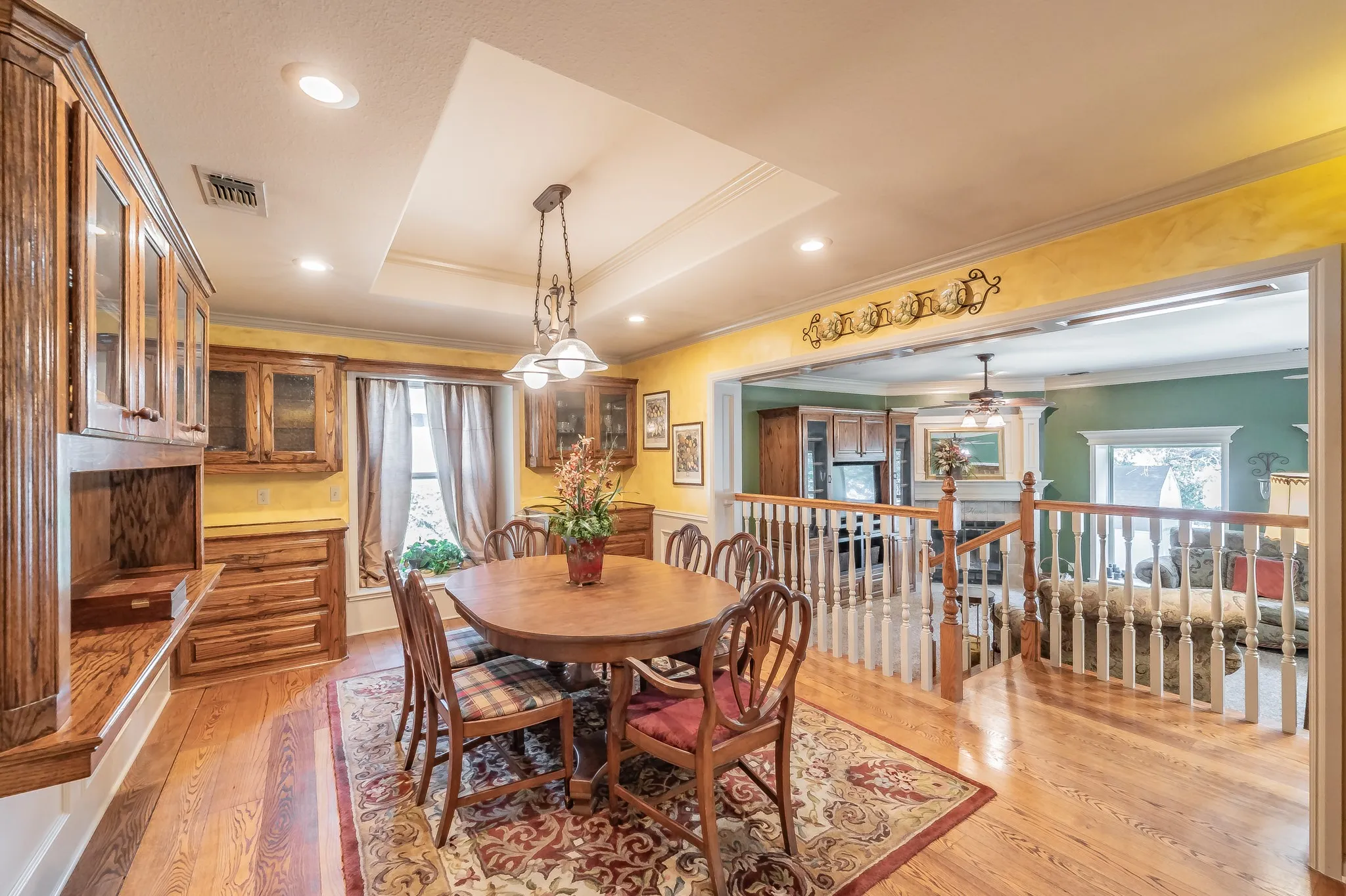 Dining room with crown molding, light real wood-flooring, a raised ceiling, recessed lighting, and a fireplace