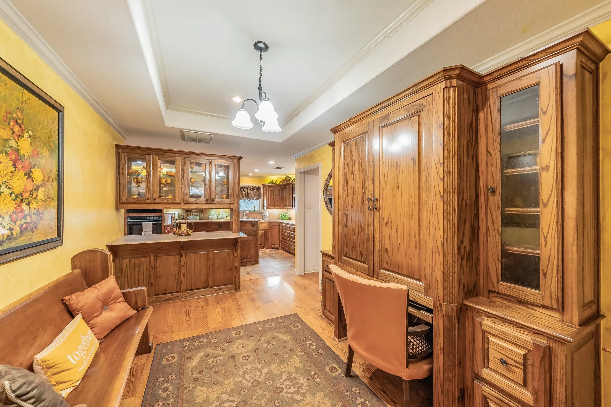 Home office featuring a custom built in desk,  ornamental molding, light wood-style flooring, a raised ceiling, and a chandelier