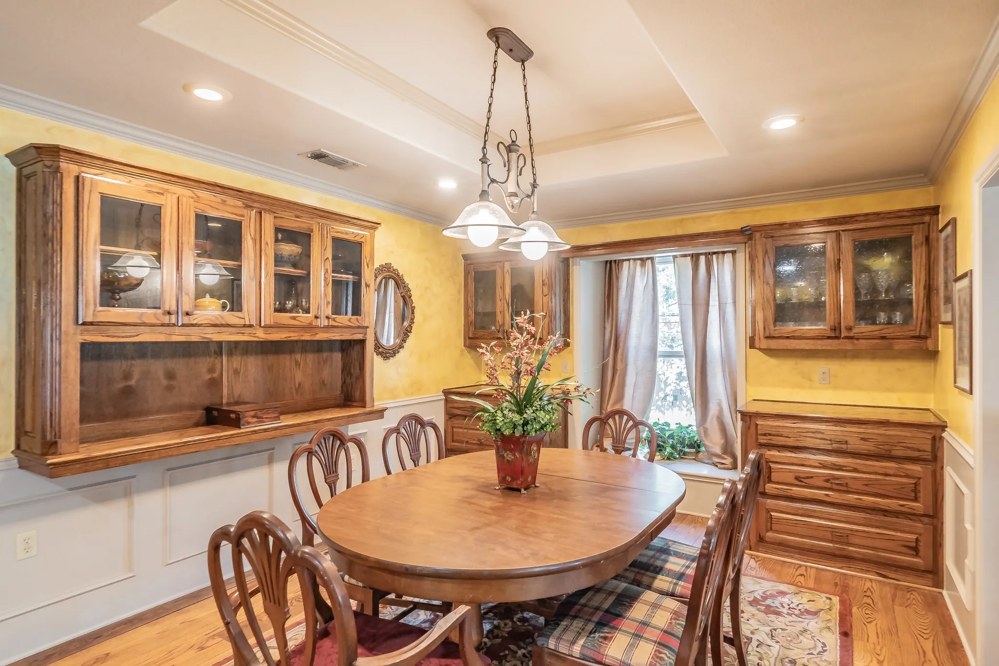 Dining room featuring ornamental molding, light wood finished floors, a raised ceiling, recessed lighting, and a wainscoted wall