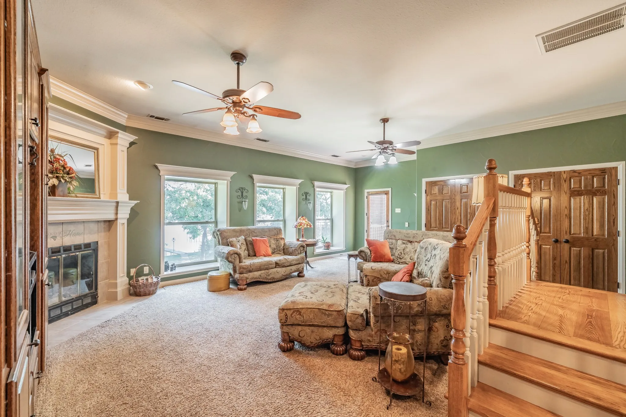 Living room featuring crown molding, a ceiling fan, a fireplace, carpet flooring, and stairs