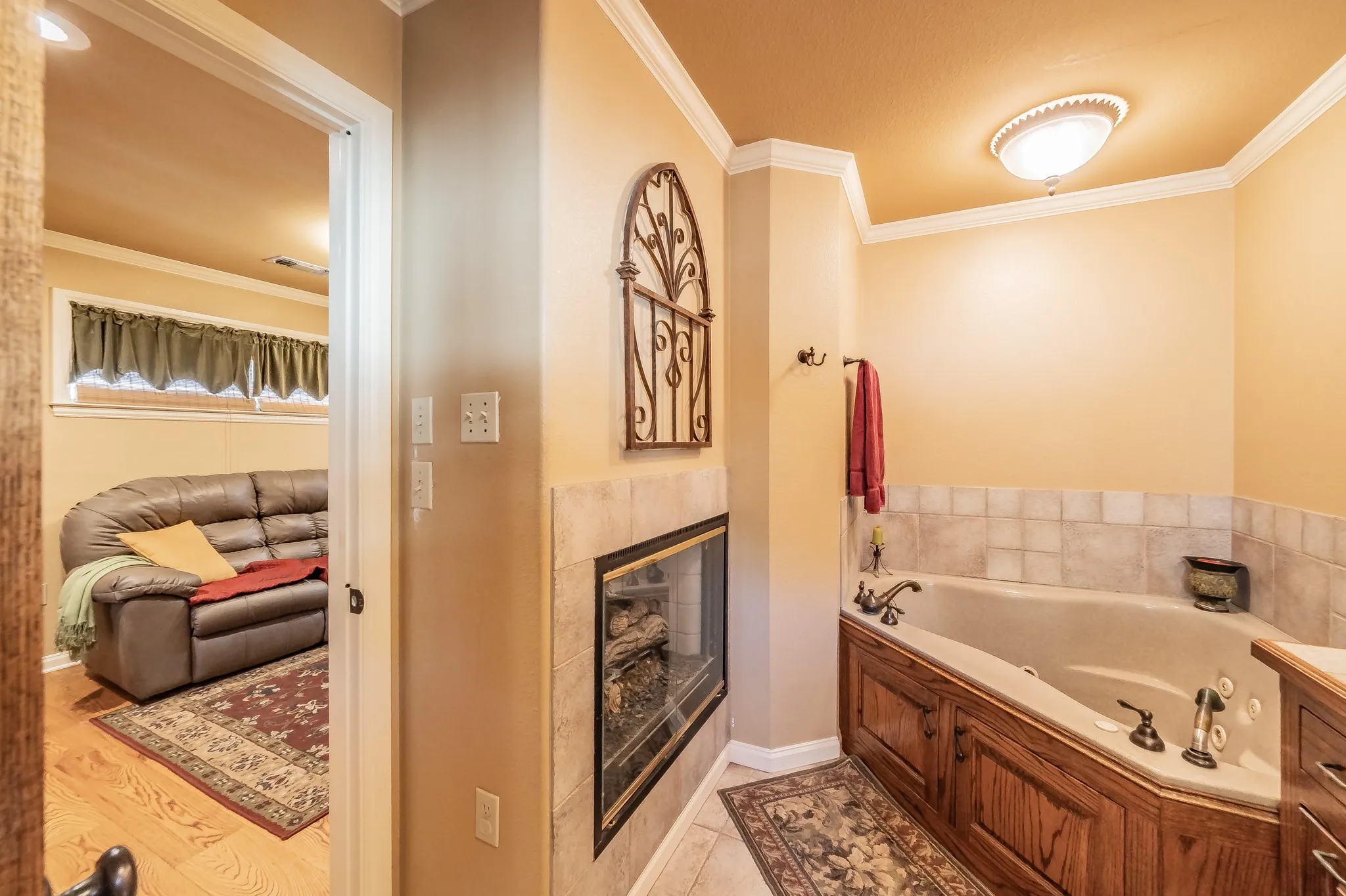 Bathroom with ornamental molding, a whirlpool tub, a fireplace, and light wood-style flooring
