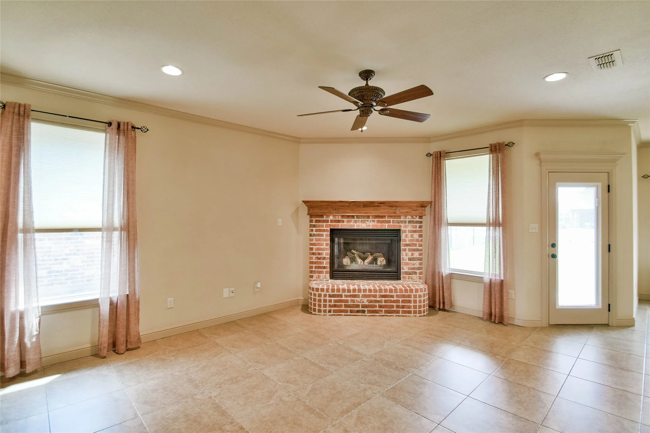 Living area with crown molding, ceiling fan, fireplace with gas logs, tile flooring