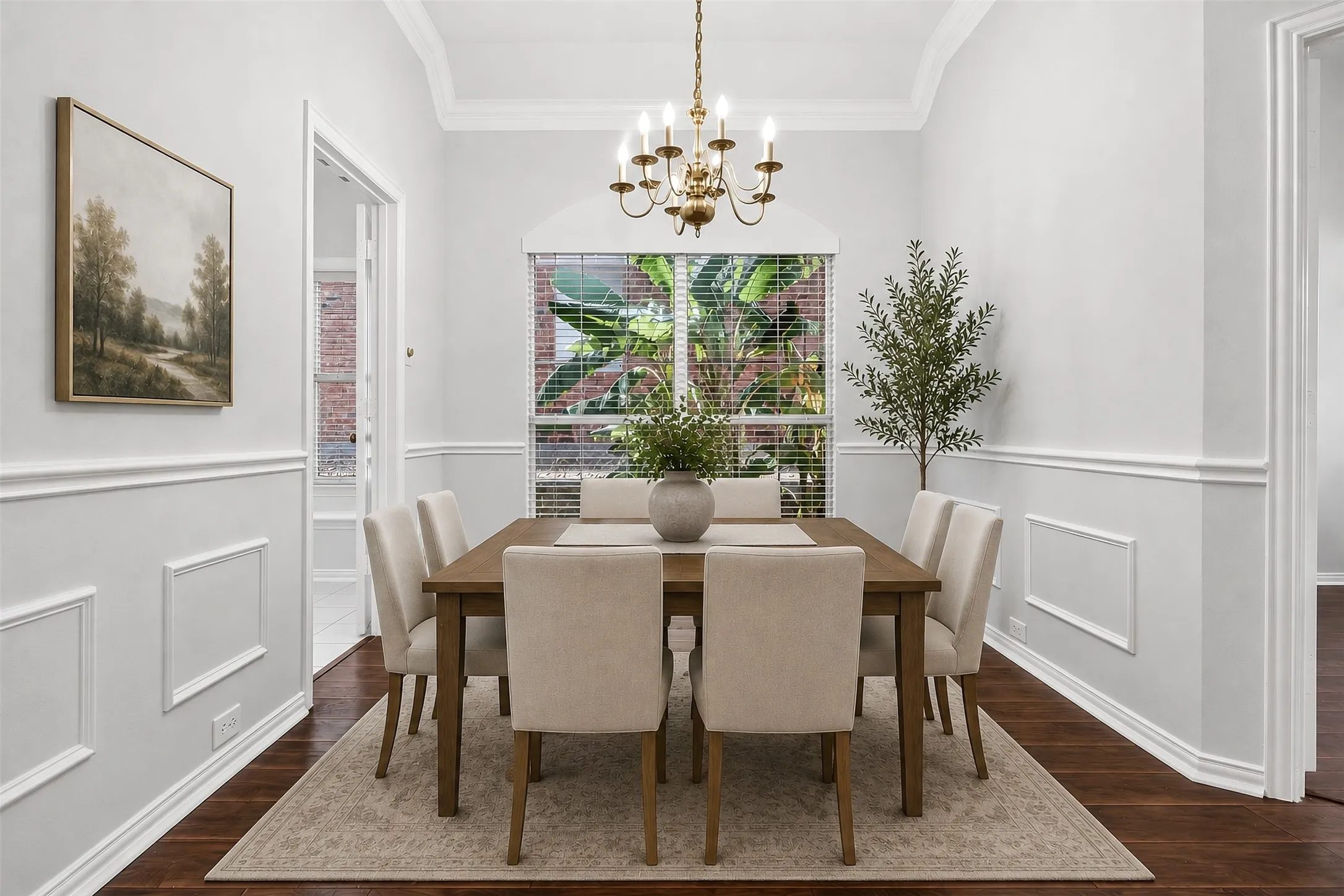 Formal dining space featuring crown molding, wainscoting, an arched window, and wood-finish flooring