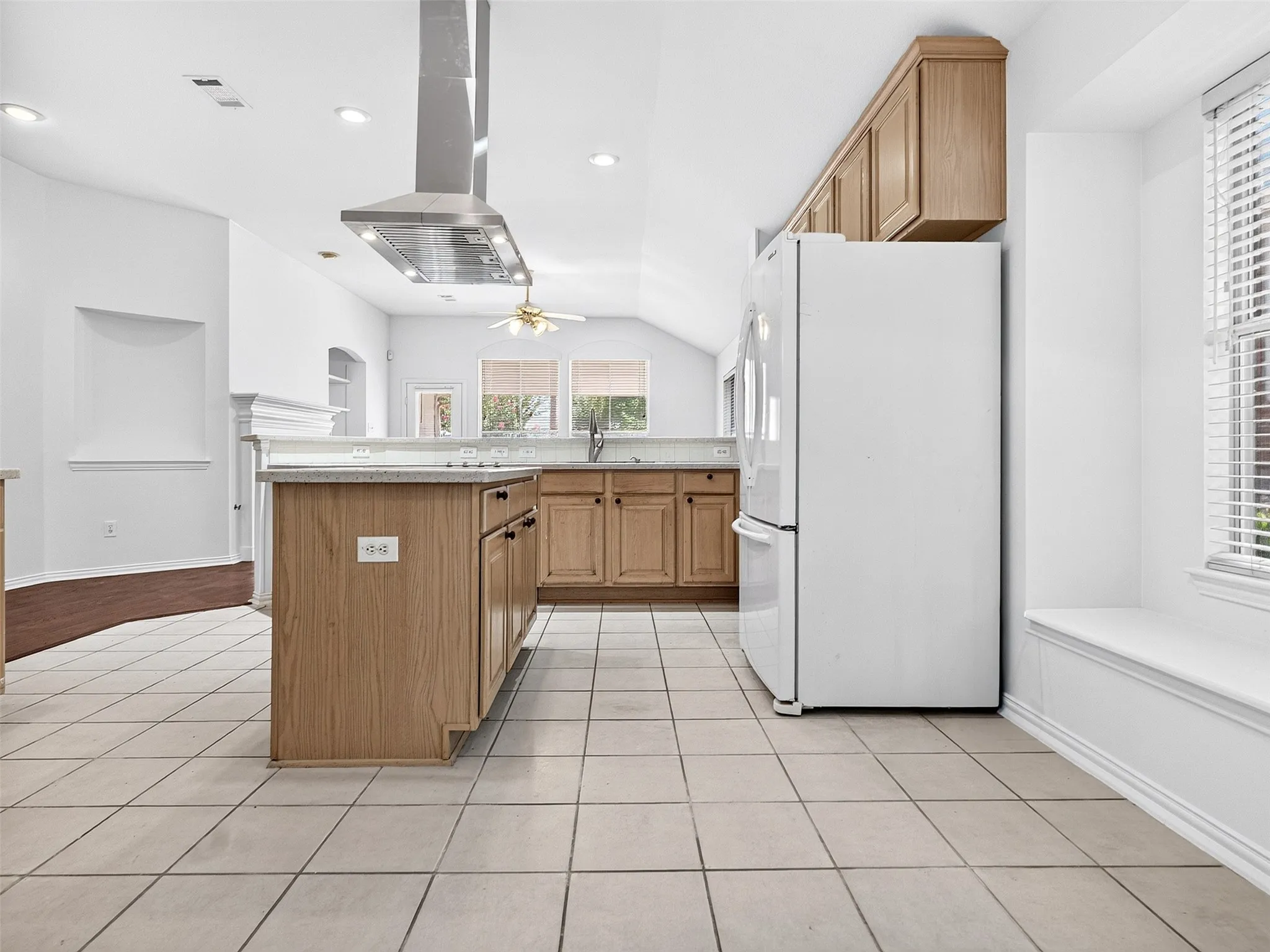 Kitchen featuring an island, tile flooring, wood cabinetry, built-in window seating, and a stainless steel range hood