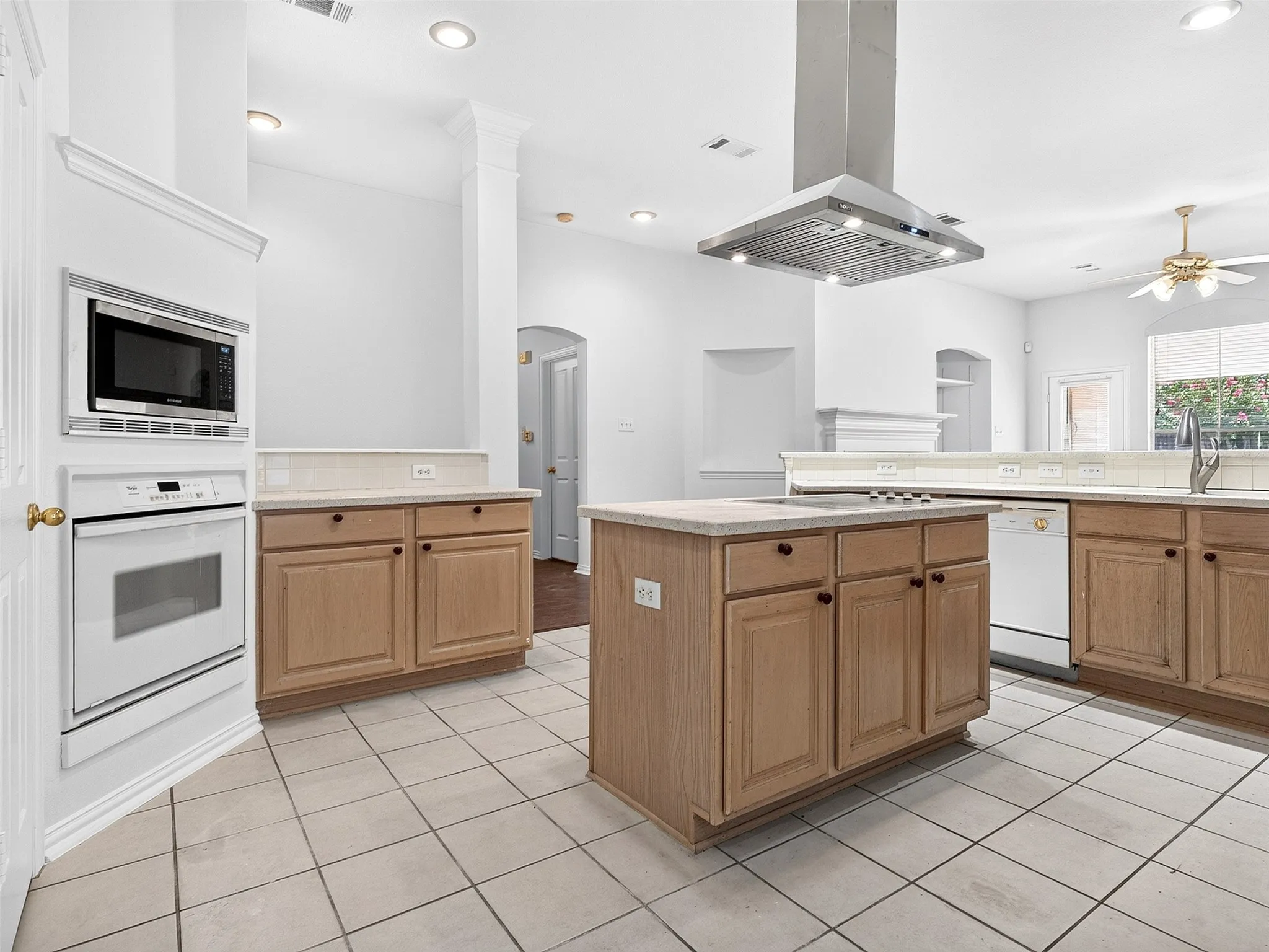 Recessed lighting, wood-finish cabinetry, tile flooring, built-in microwave, and stainless steel range hood