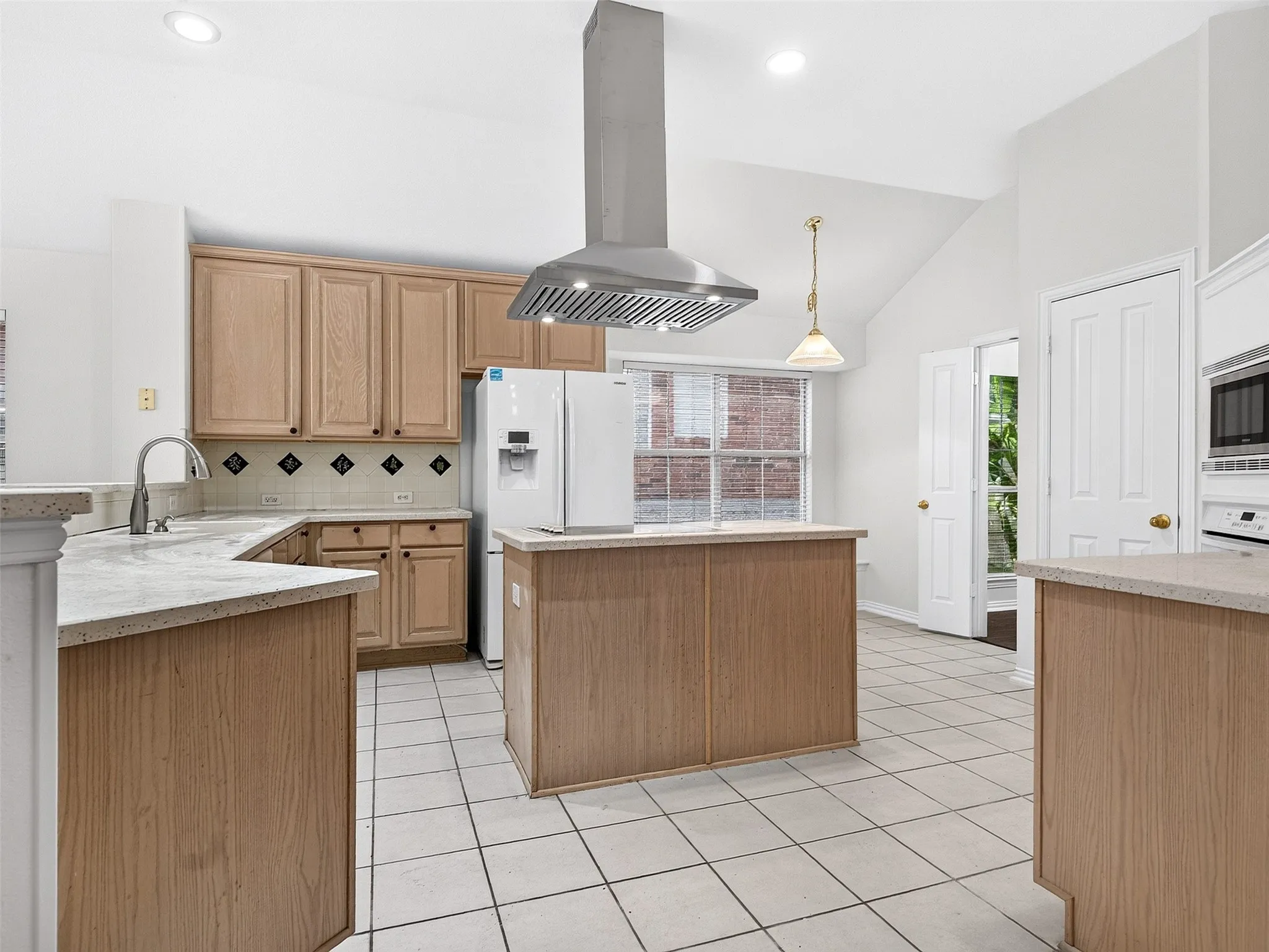 Kitchen featuring light wood cabinetry, light-colored countertops, a stainless steel range hood, and tile flooring