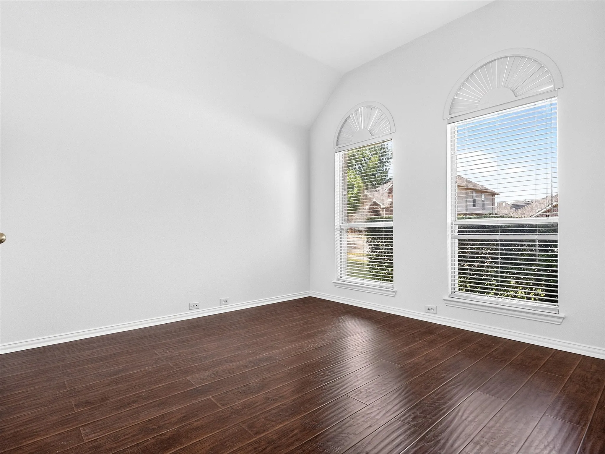 Vaulted ceiling, two arched windows with blinds, wood-finish flooring, and white baseboards