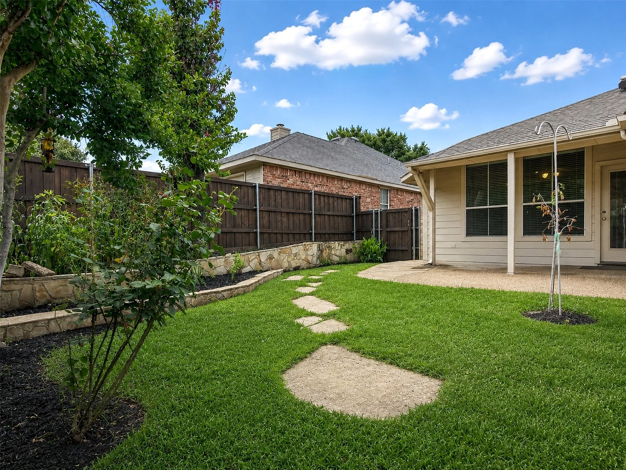 Expansive backyard featuring a stone retaining wall, mature perimeter fencing, and a stepping stone pathway