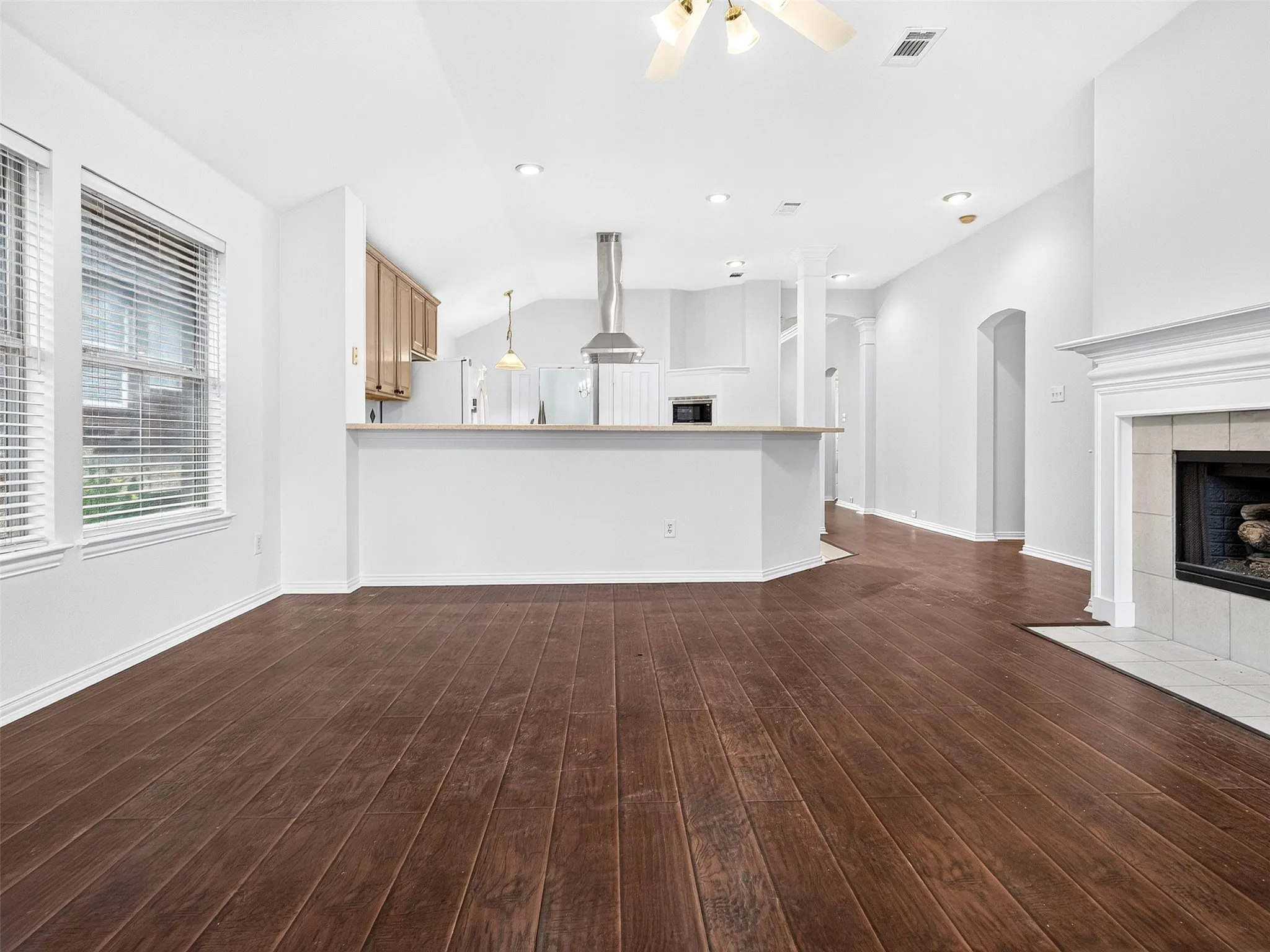 Wood-finish flooring throughout, vaulted ceiling, built-in fireplace with white mantel, recessed lighting, and kitchen with stainless steel range hood