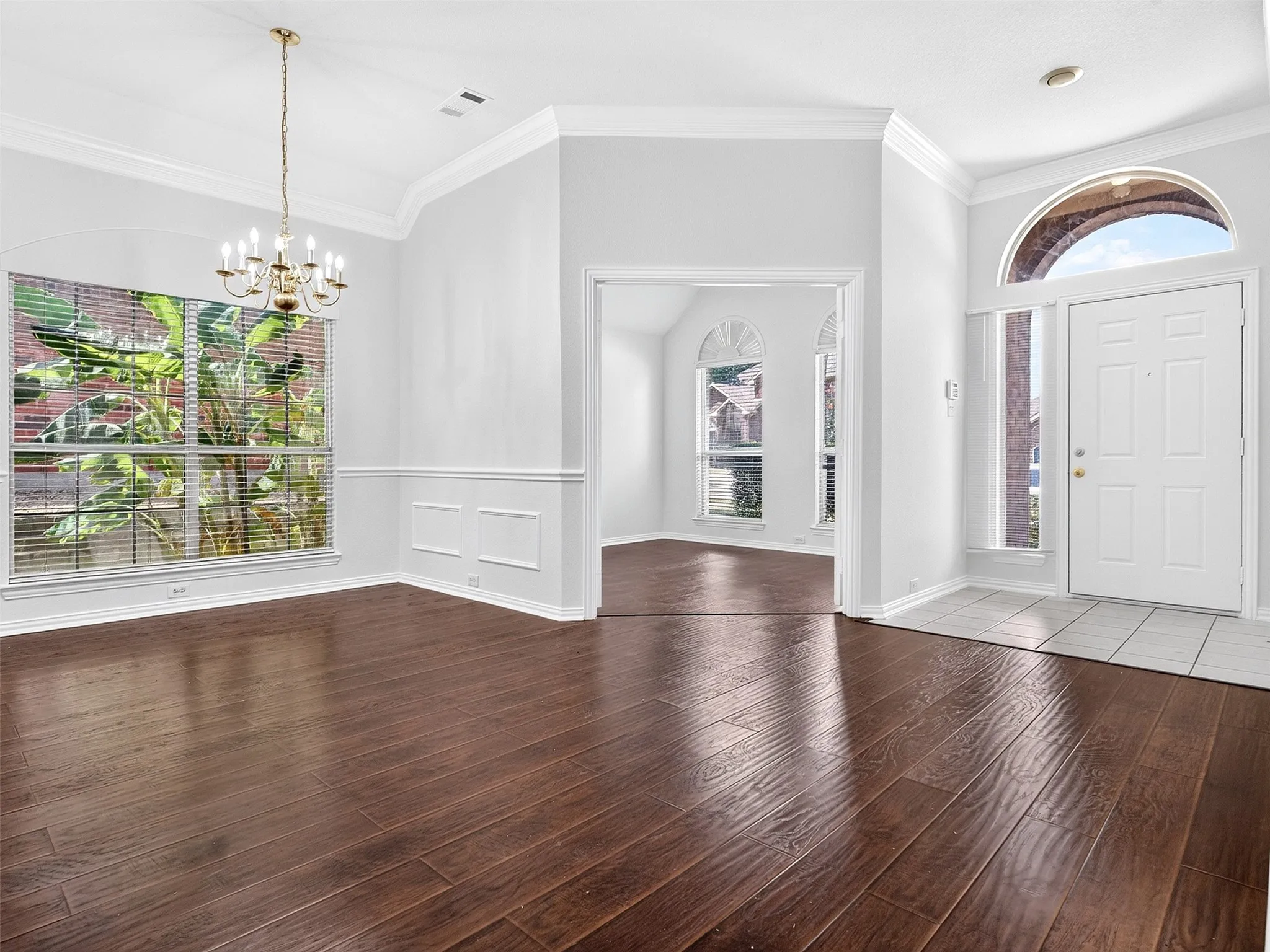 Wood-finish flooring, wainscoting, crown molding, and a multi-arm chandelier