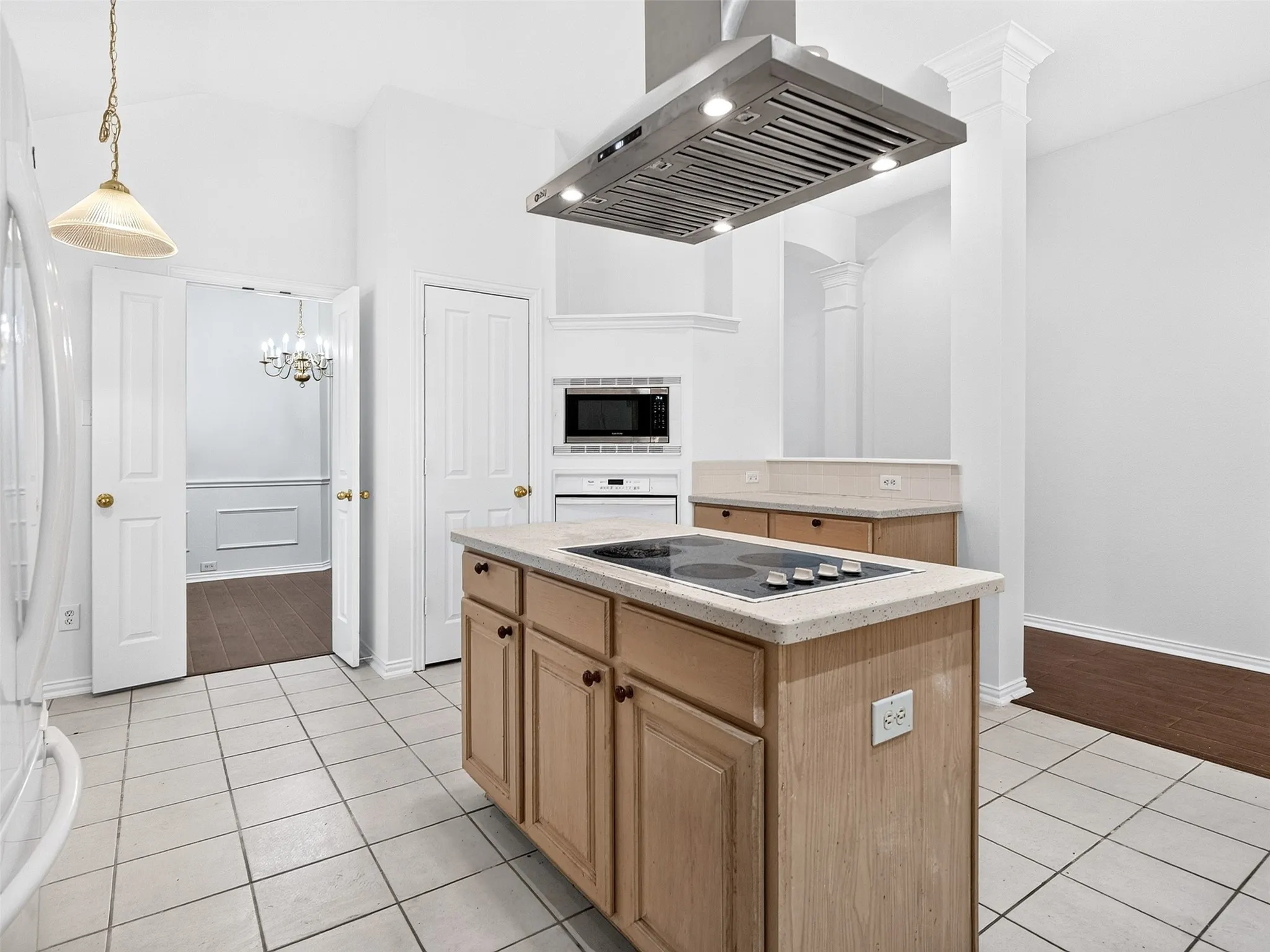 Kitchen featuring an island with an integrated cooktop, stainless steel range hood, built-in microwave, and tile flooring