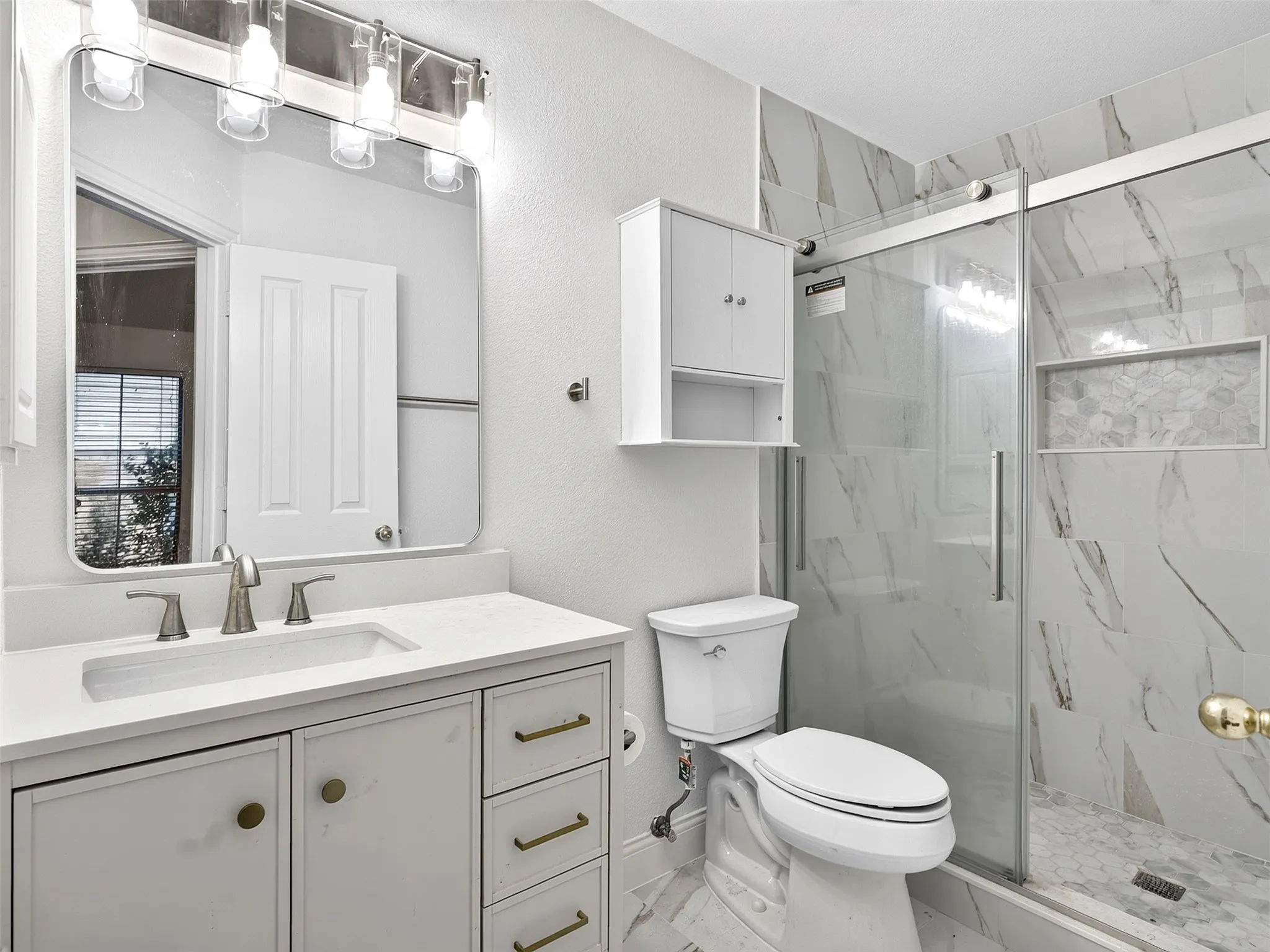 White vanity with brass hardware and integrated sink, quartz countertop, framed mirror, and chrome vanity lighting