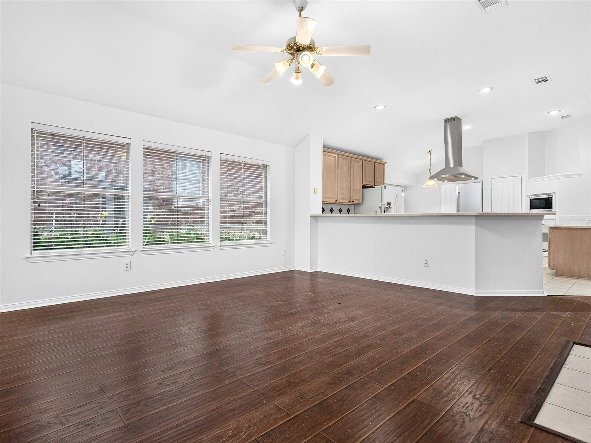 Open-concept living area featuring wood-finish flooring, a ceiling fan, and three large windows