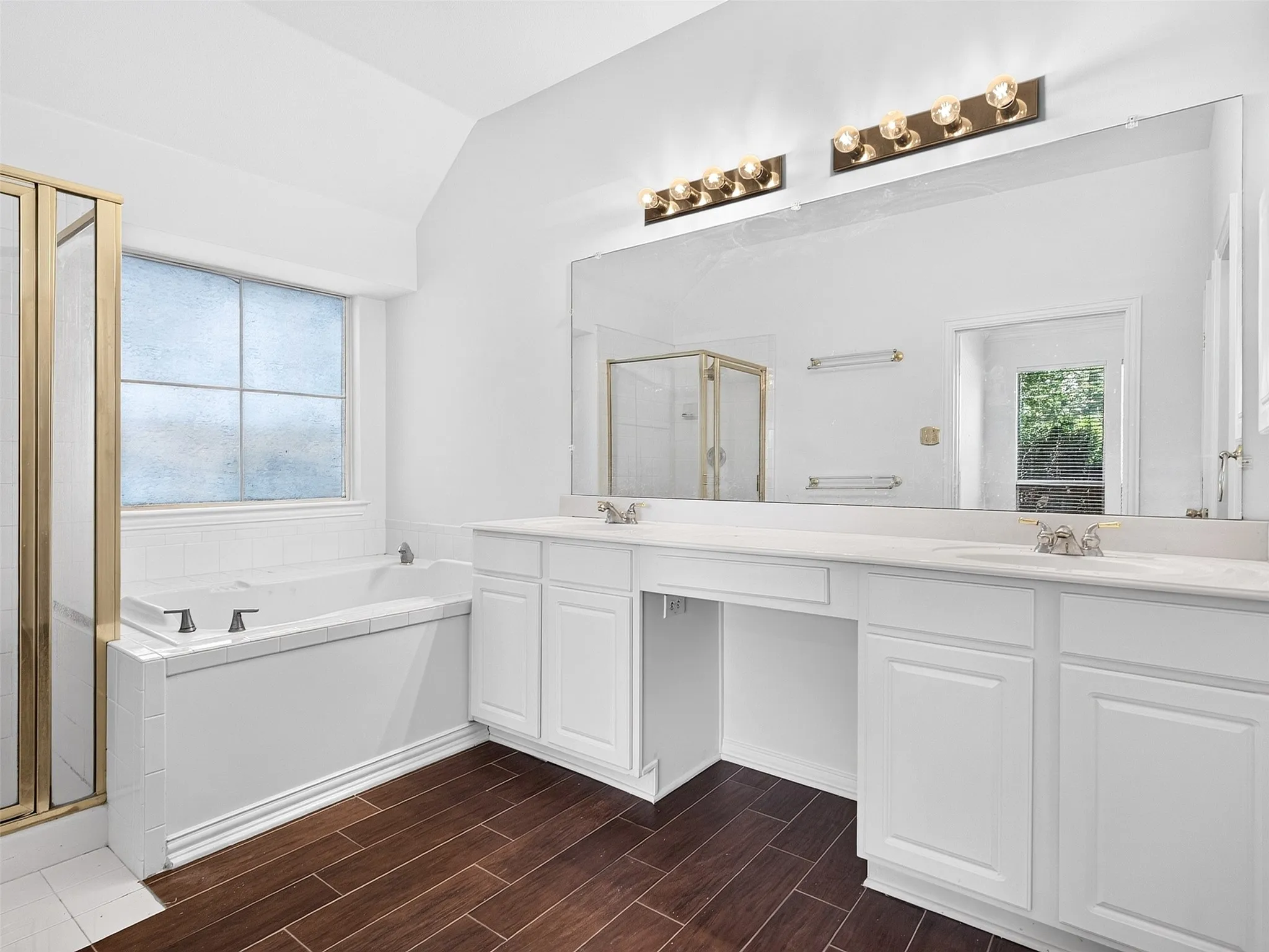 Dual vanity with white cabinetry, built-in bathtub, and separate shower with brass-finish enclosure