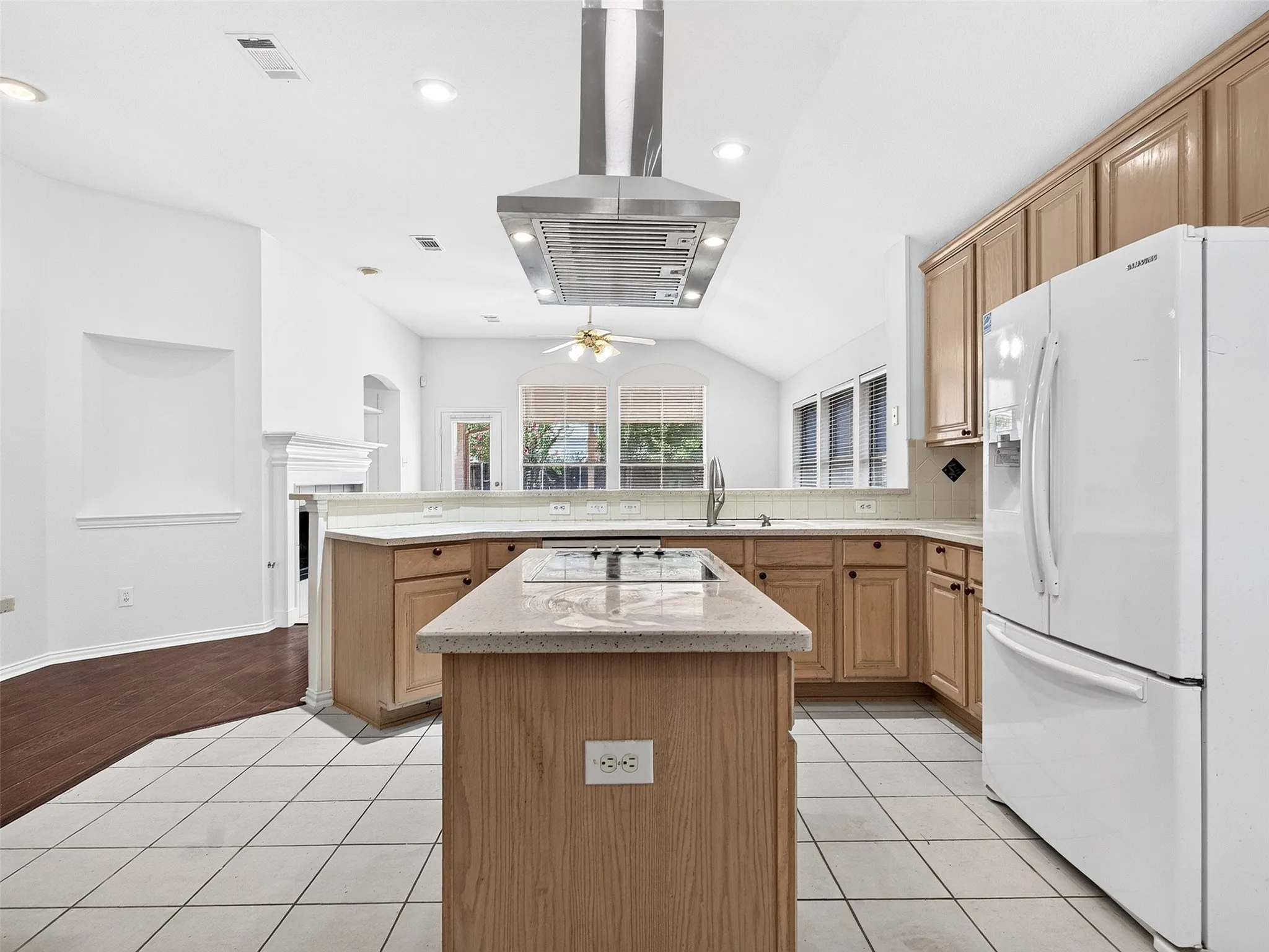 Kitchen featuring a central island with a built-in cooktop, stainless steel range hood, light-toned cabinetry, light-colored countertops, and tile flooring