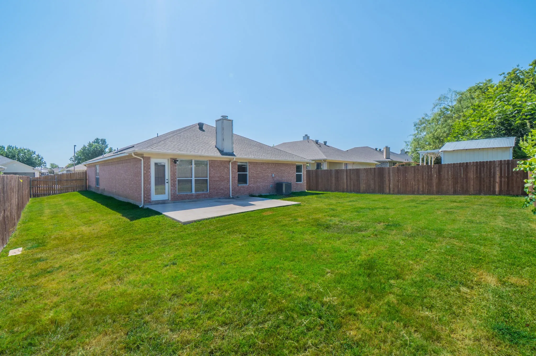 Expansive lawn with a concrete patio, brick exterior, and wood fencing