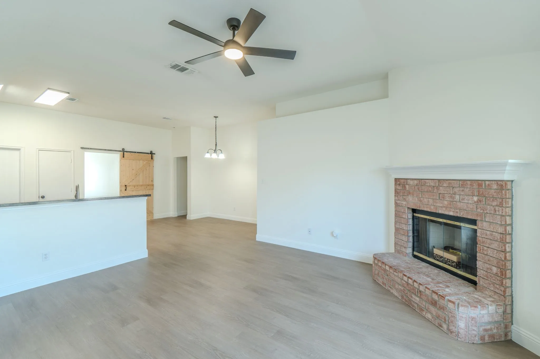 Spacious living area featuring wood-finish flooring, a ceiling fan, and a brick fireplace