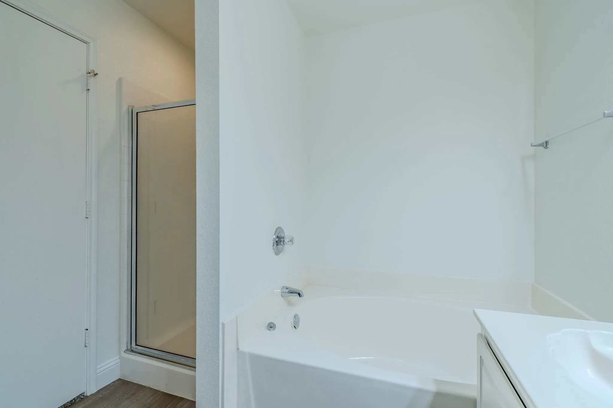 Recessed corner bathtub with chrome fixtures, enclosed shower, and a white vanity with an integrated sink