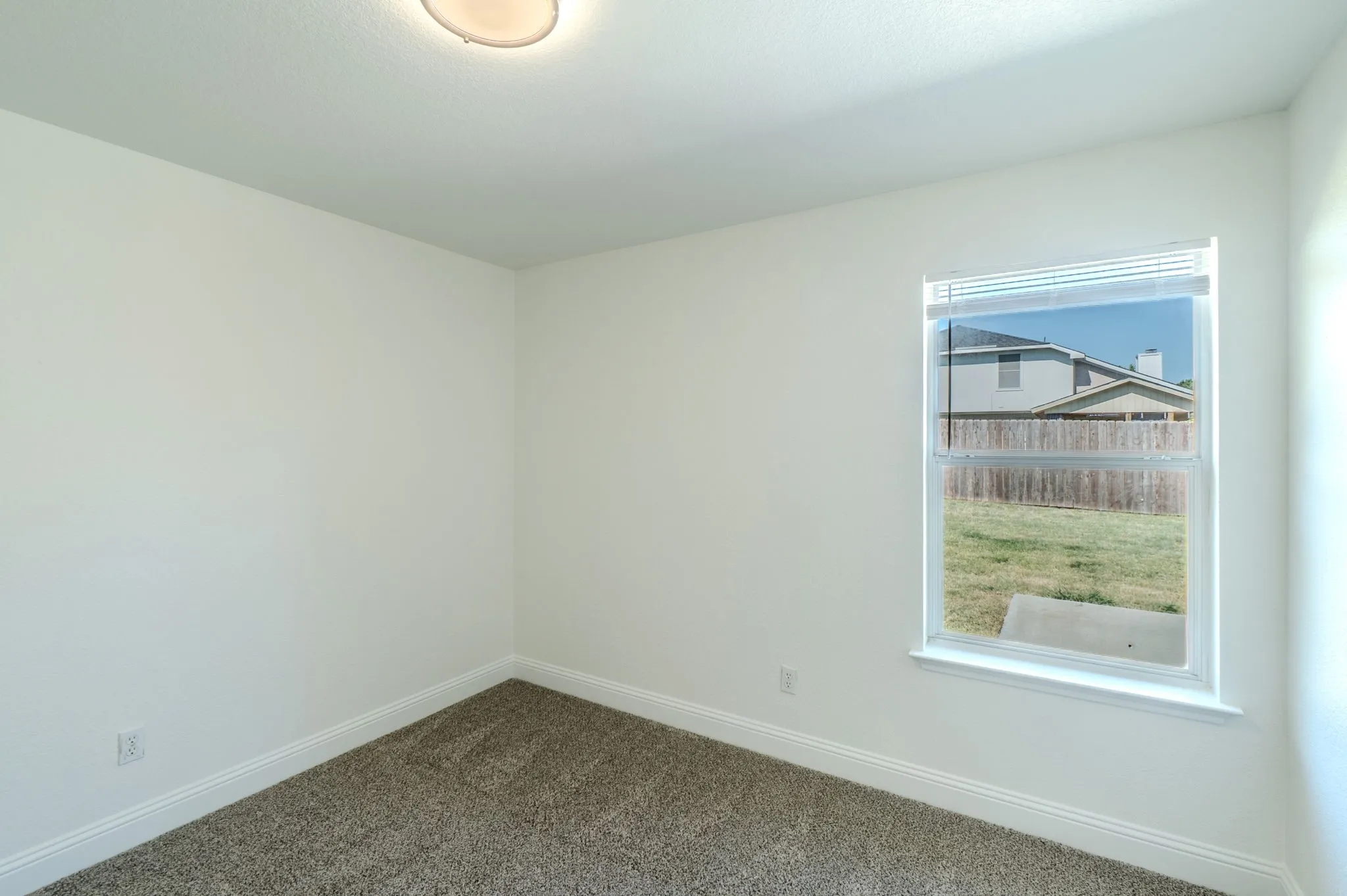 Recessed ceiling light, neutral wall paint, single window with blinds, light-colored carpet, and white trim